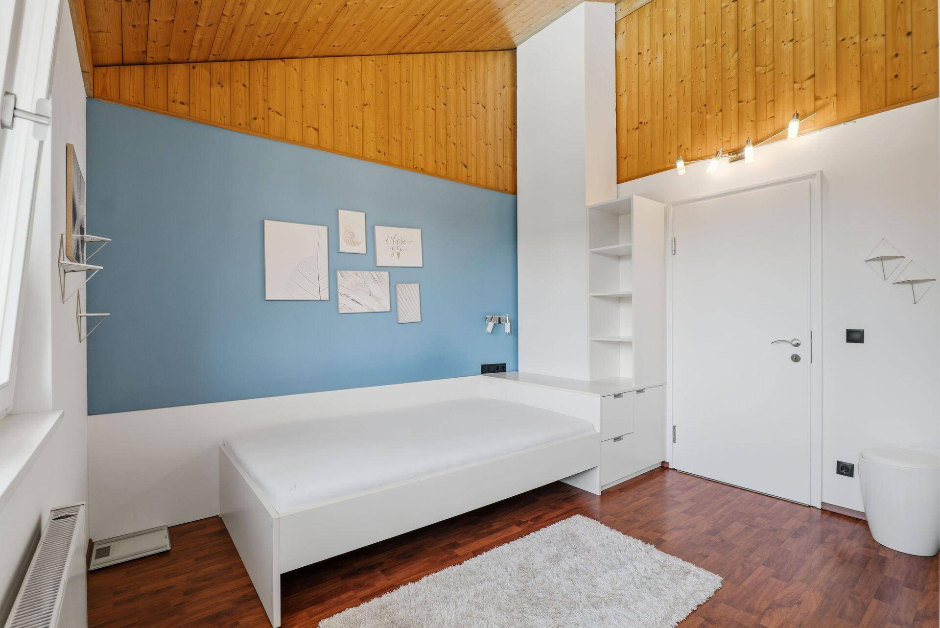 Modernes Schlafzimmer mit blauer Akzentwand, Holzdachschräge und Einzelbett.