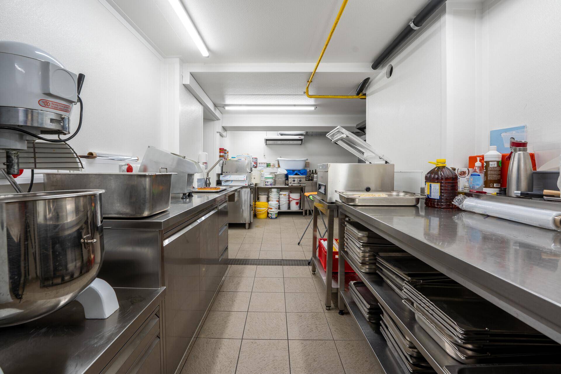 Professionelle Großküche mit Edelstahloberflächen, industriellen Geräten und Fliesenboden für den Betrieb.