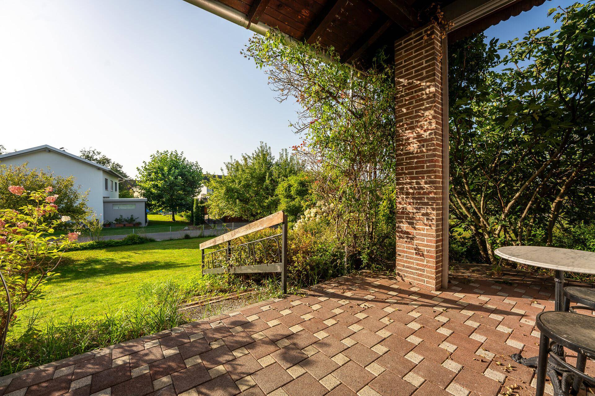 Überdachte Terrasse mit Ziegelpfeilern und gepflastertem Boden, ideal für Mahlzeiten im Freien.