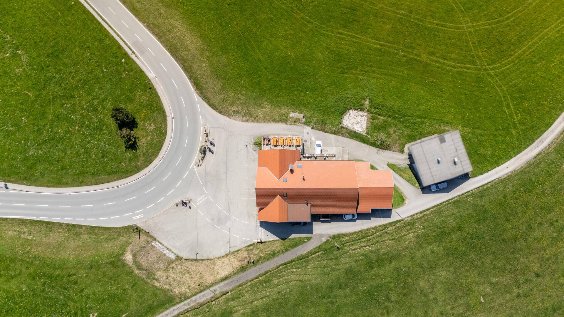 Luftaufnahme eines Gebäudekomplexes mit roten Dächern, umgeben von grünen Wiesen und Straßen.