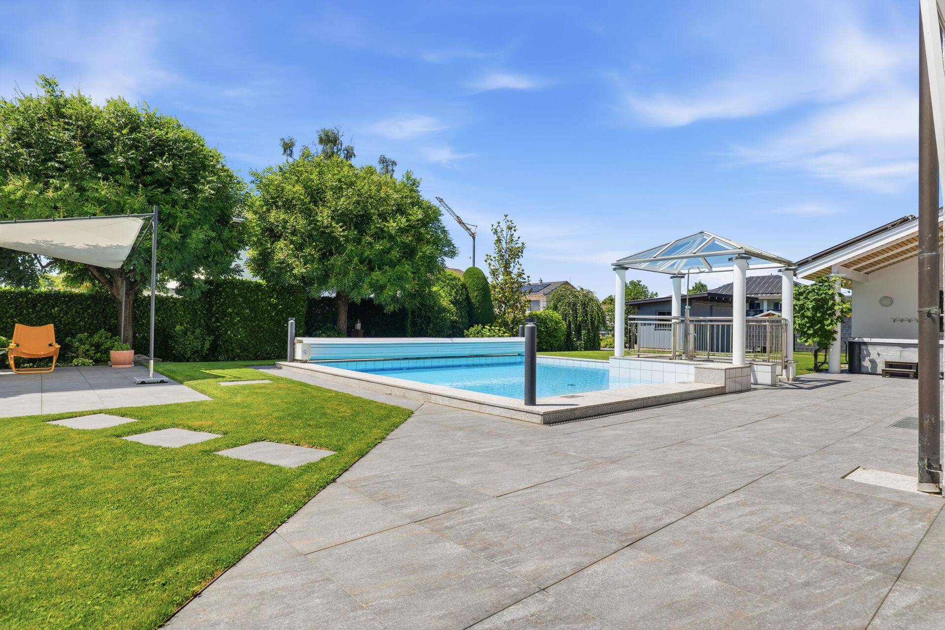 Gepflegter Garten mit Pool, Liegefläche und schattenspendendem Sonnensegel.