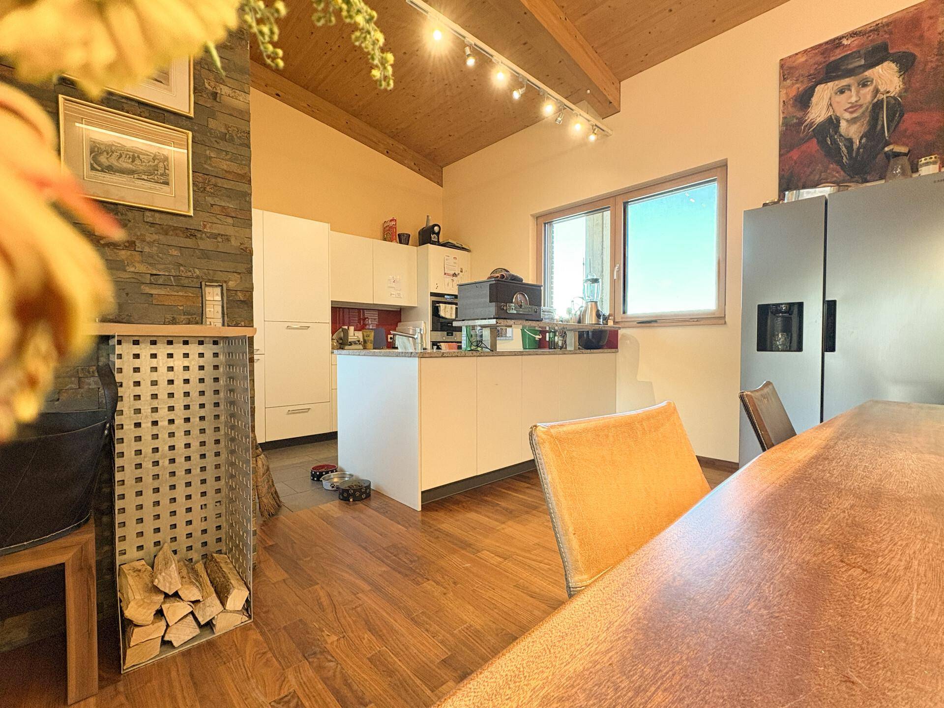 Helle Küche mit weißen Schränken, Holzdecke und einem Holzofen im Hintergrund.