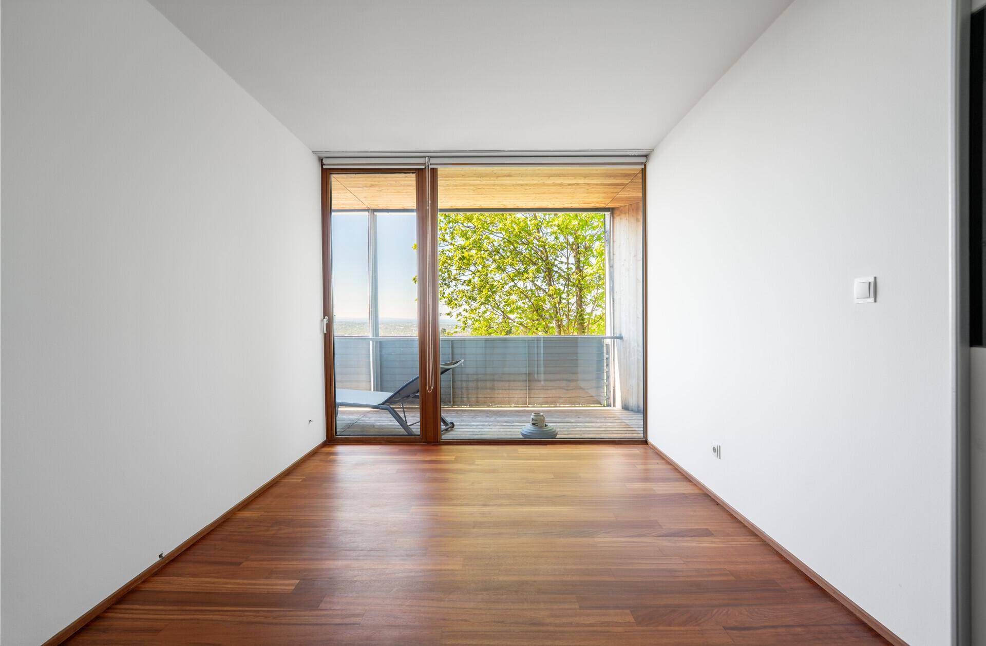 Helles Zimmer mit Holzboden und großer Schiebetür zum Balkon mit Weitblick.