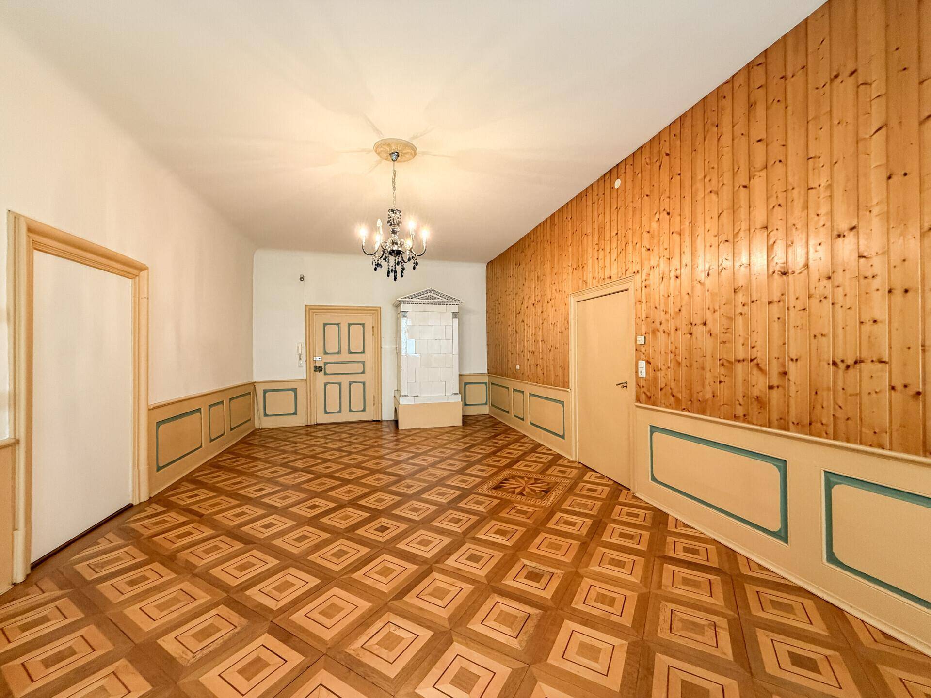 Geräumiger Flur mit Holztäfelung, Parkettboden und traditionellem Kachelofen.