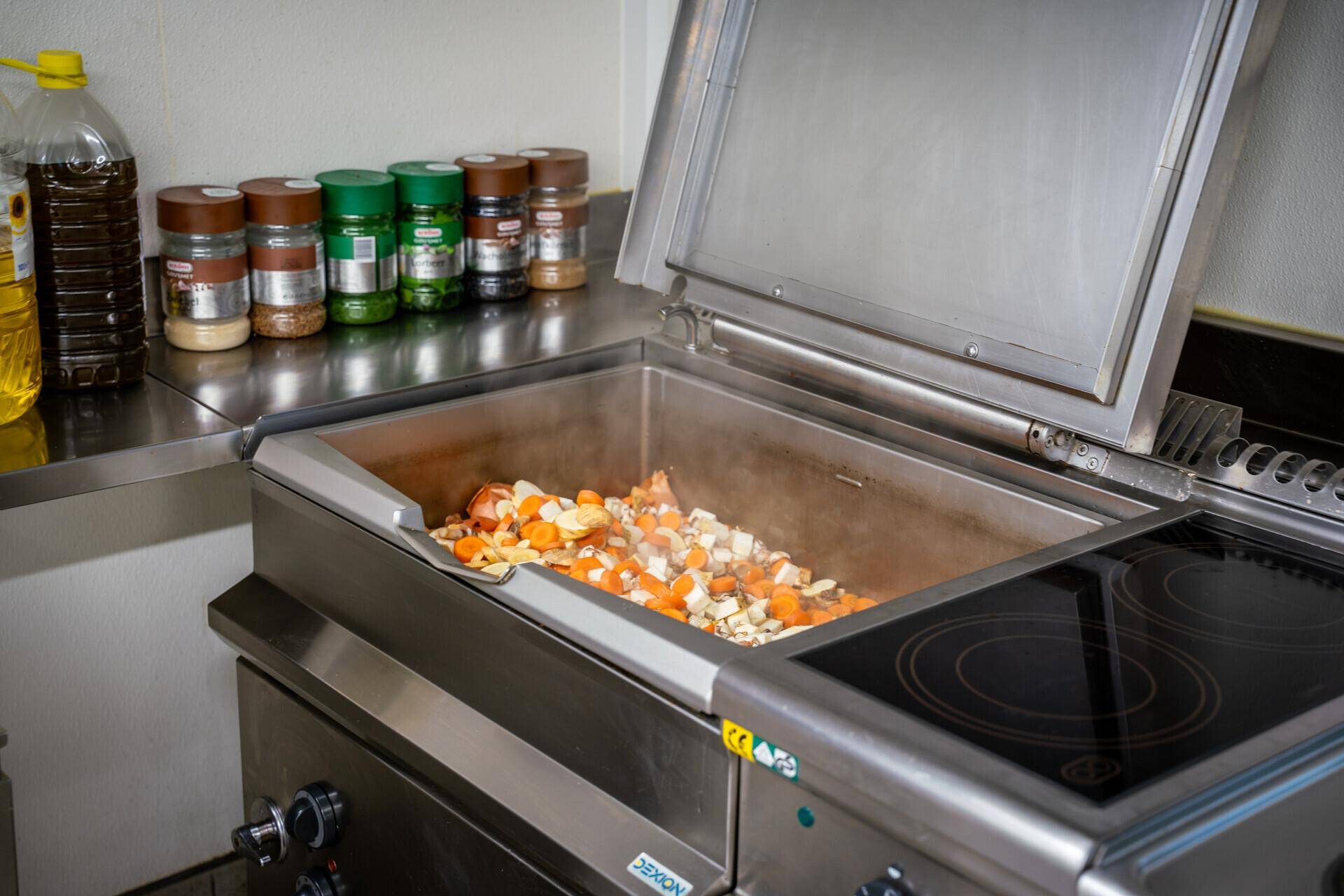 Großer Kochtopf mit frischem Gemüse auf einem Induktionskochfeld in einer professionellen Küche.