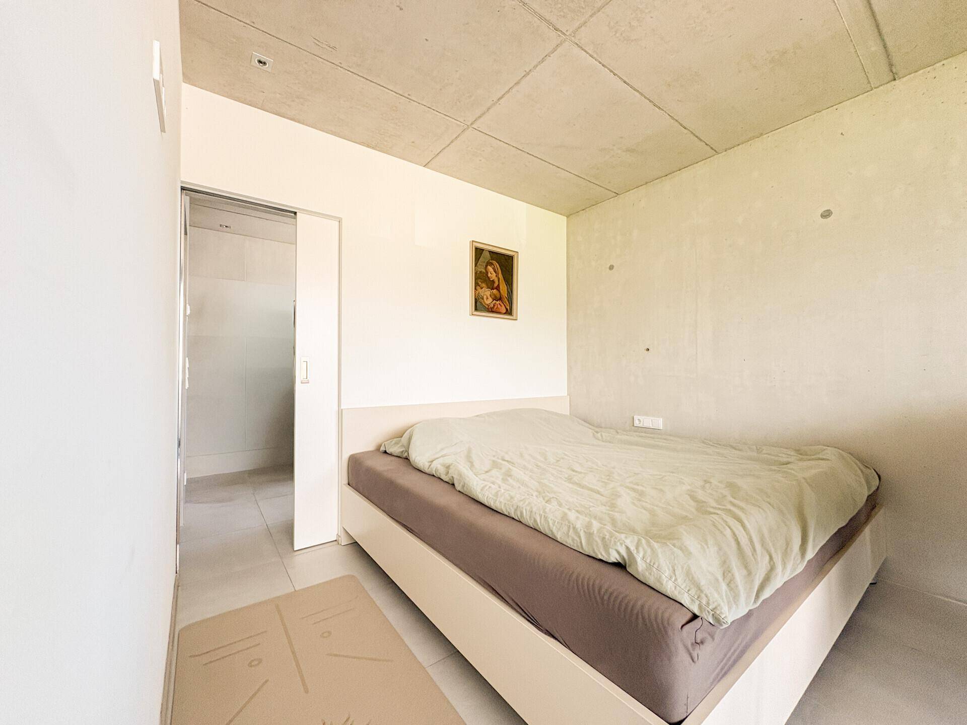 Modernes Schlafzimmer mit minimalistischem Design, Fliesenboden und Zugang zu einem angrenzenden Badezimmer.