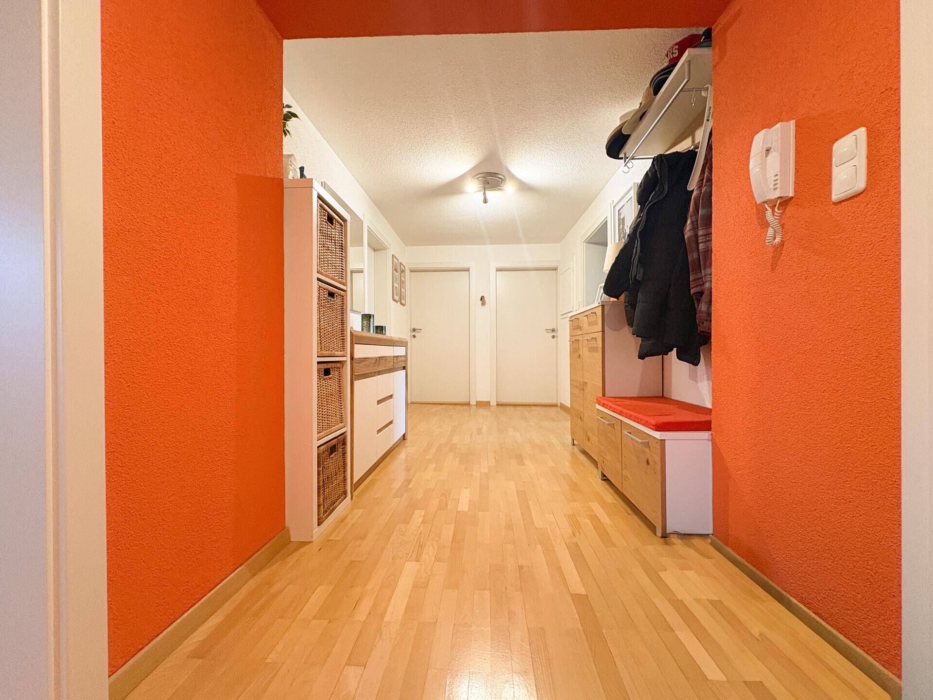 Heller Flur mit orangefarbenen Wänden, Holzboden und Garderobenbereich.