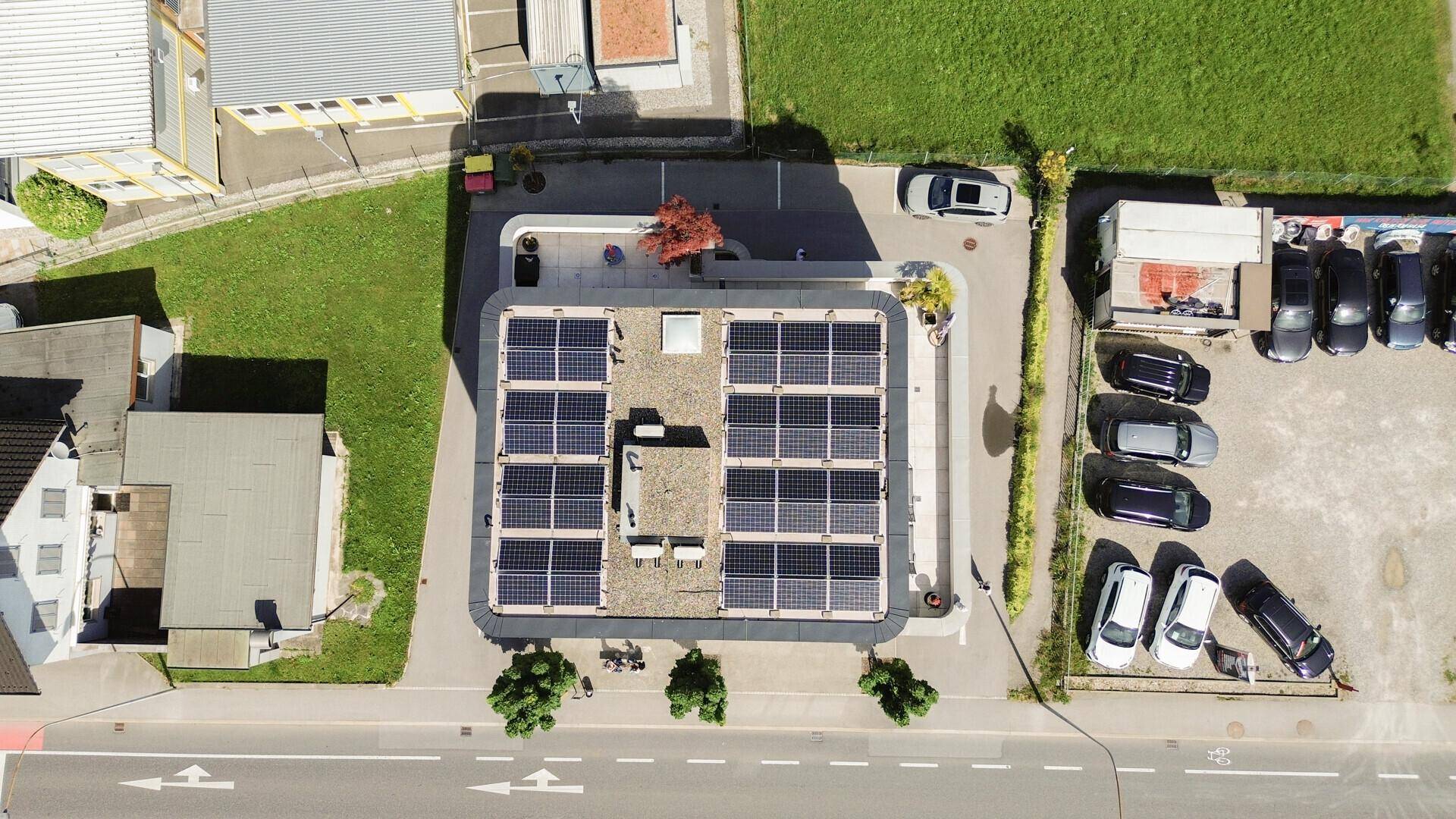 Draufsicht auf das Flachdach mit Photovoltaikanlage und umliegenden Parkplätzen und Grünflächen.