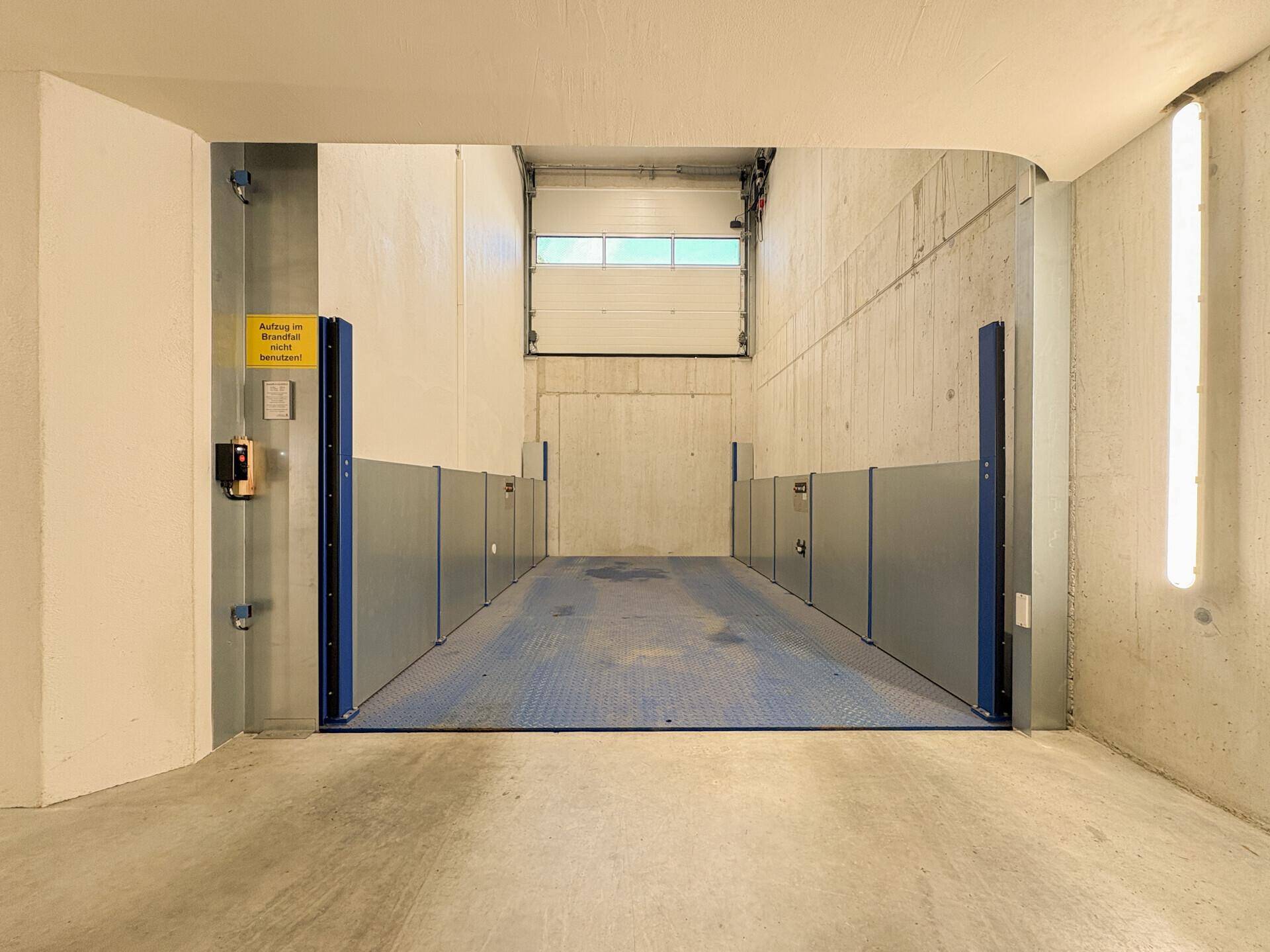 Moderner Autolift in einer Tiefgarage mit Betonwänden und Beleuchtung.
