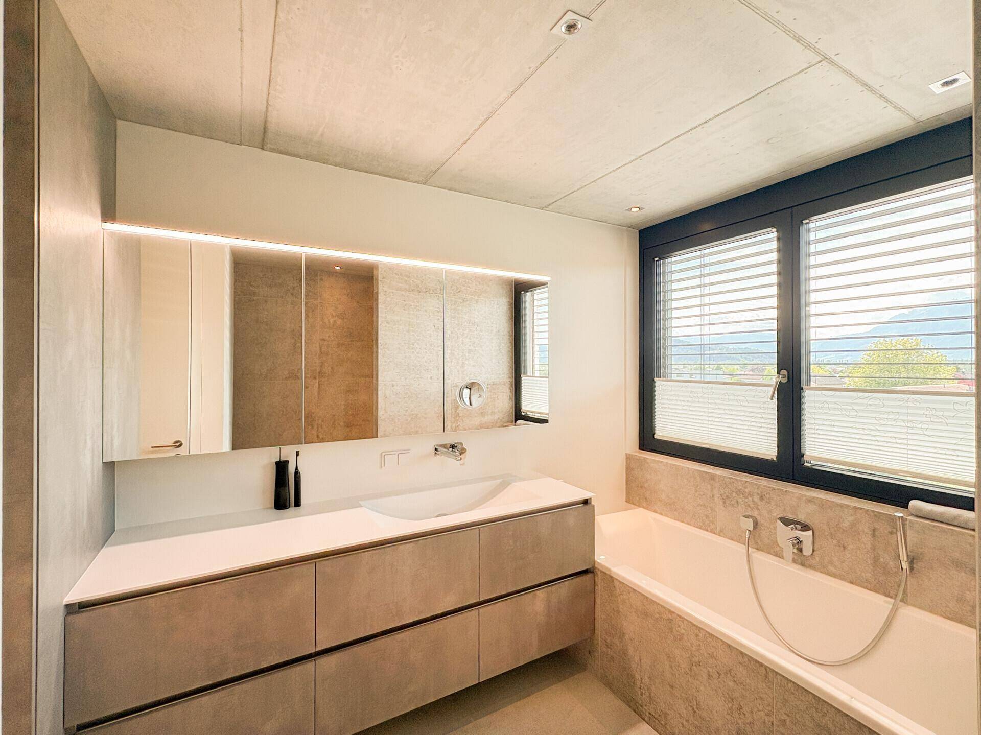 Helles Badezimmer mit Badewanne, großem Waschtisch und Fenster mit Bergblick.