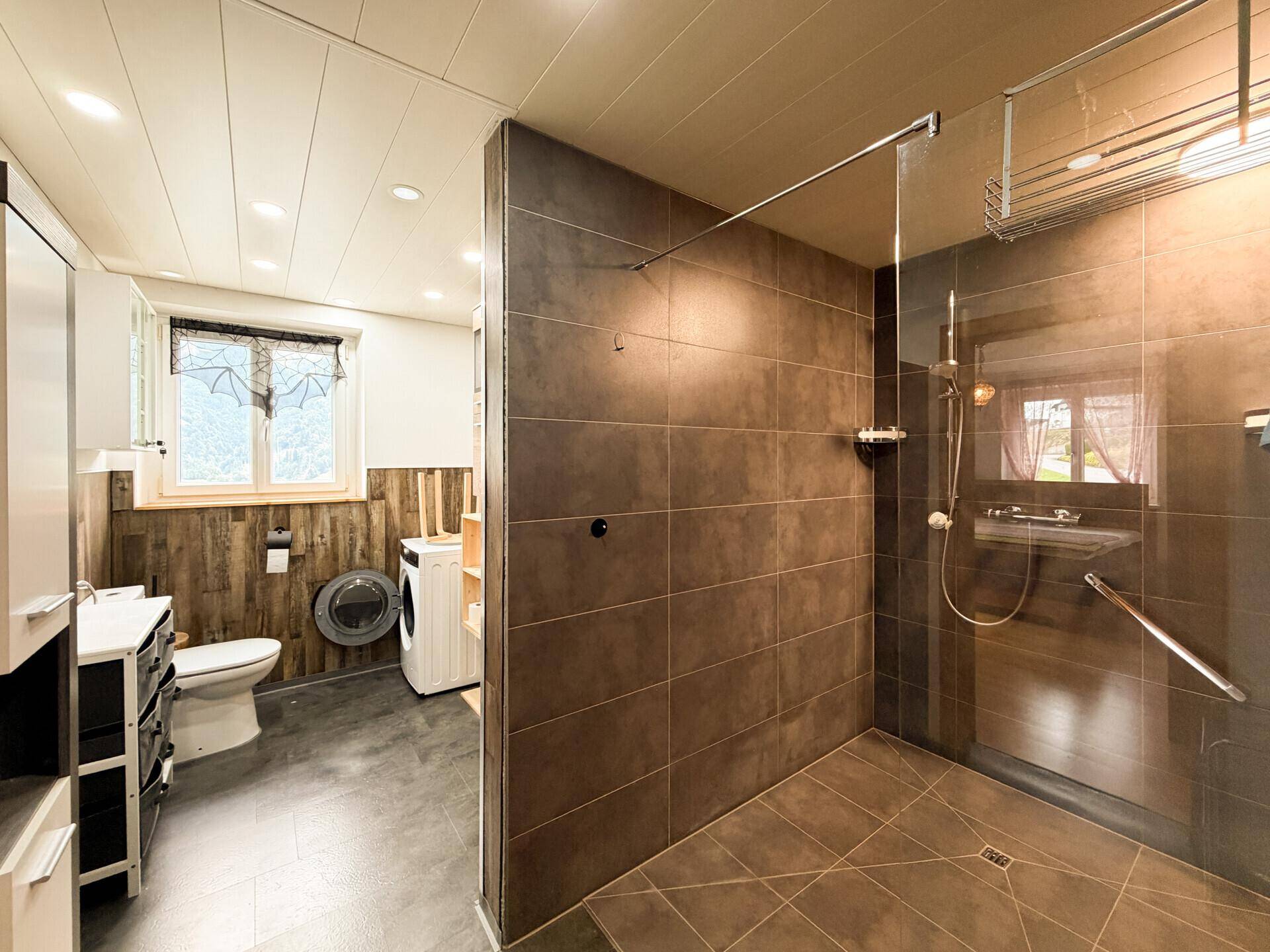 Modernes Badezimmer mit ebenerdiger Dusche, Waschmaschine und Holzverkleidung.