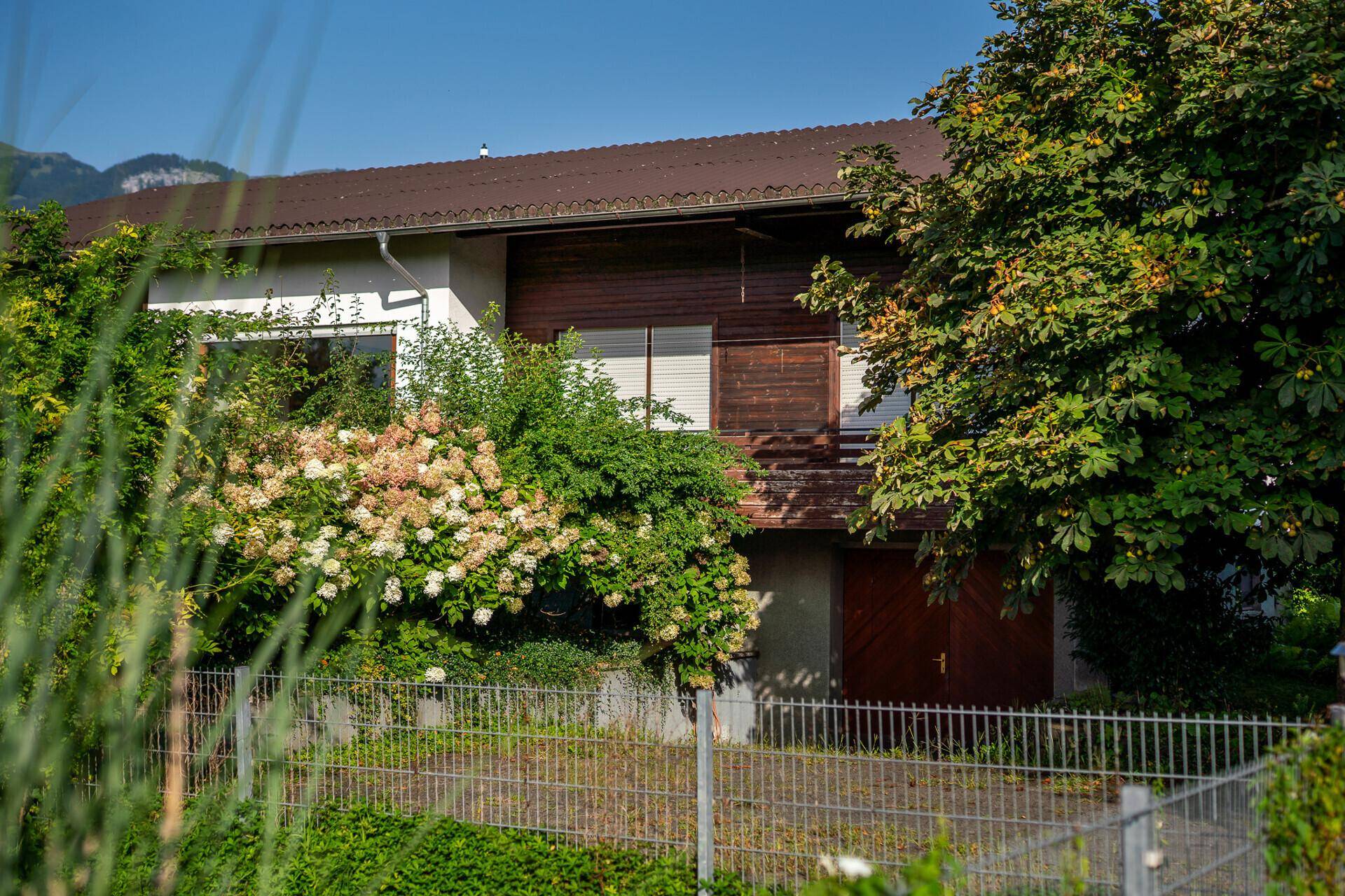 Hausfassade mit integrierter Garage und üppiger Bepflanzung im Vordergrund.