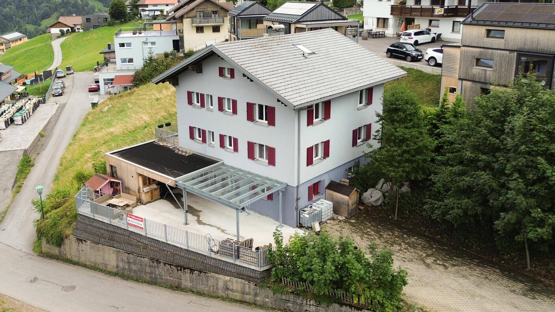 Vogelperspektive des Hauses mit Carport, umgeben von grünen Hügeln und weiteren Gebäuden.