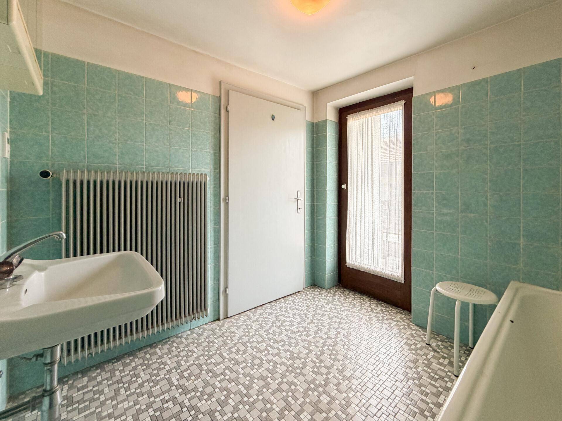 Retro-Badezimmer mit türkisfarbenen Wandfliesen, Mosaikboden und einem Fenster.