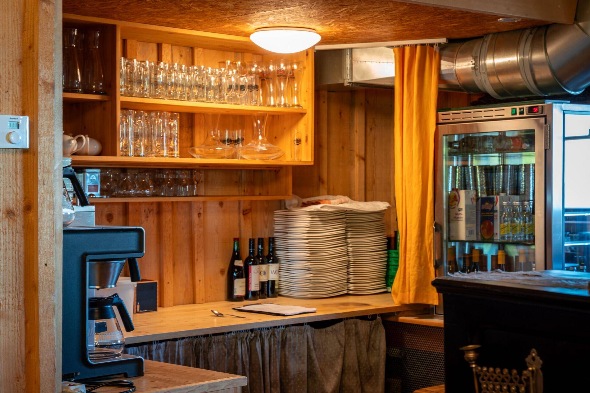 Funktionale Holzküche mit vielen Gläsern, Geschirr und einem Kühlschrank für den Gastronomiebetrieb.