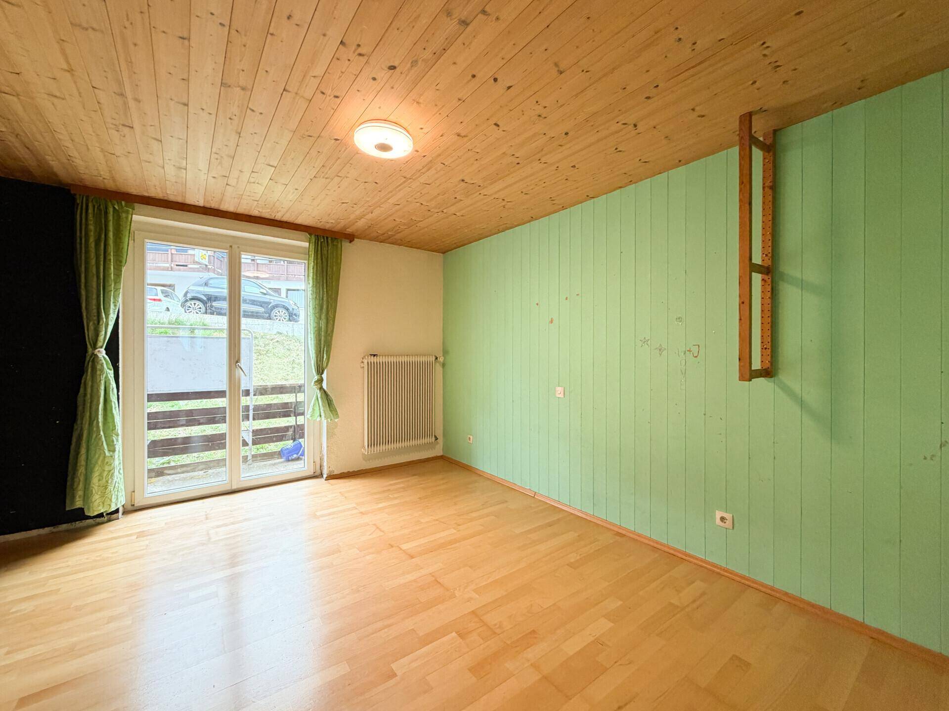 Helles Zimmer mit Holzboden, grüner Wandverkleidung und Zugang zu einem Außenbereich.