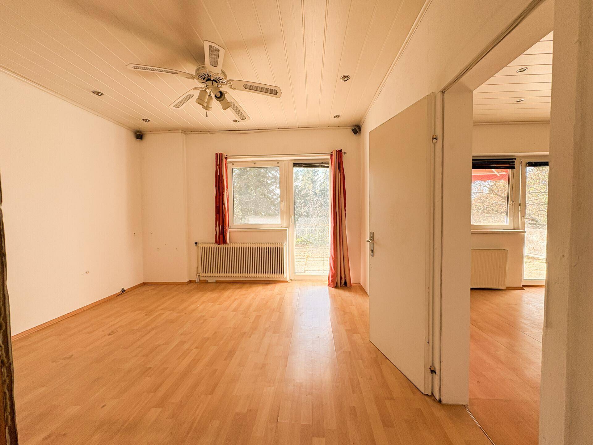 Geräumiges Wohnzimmer mit Holzfußboden, Deckenventilator und Zugang zu einem Außenbereich.