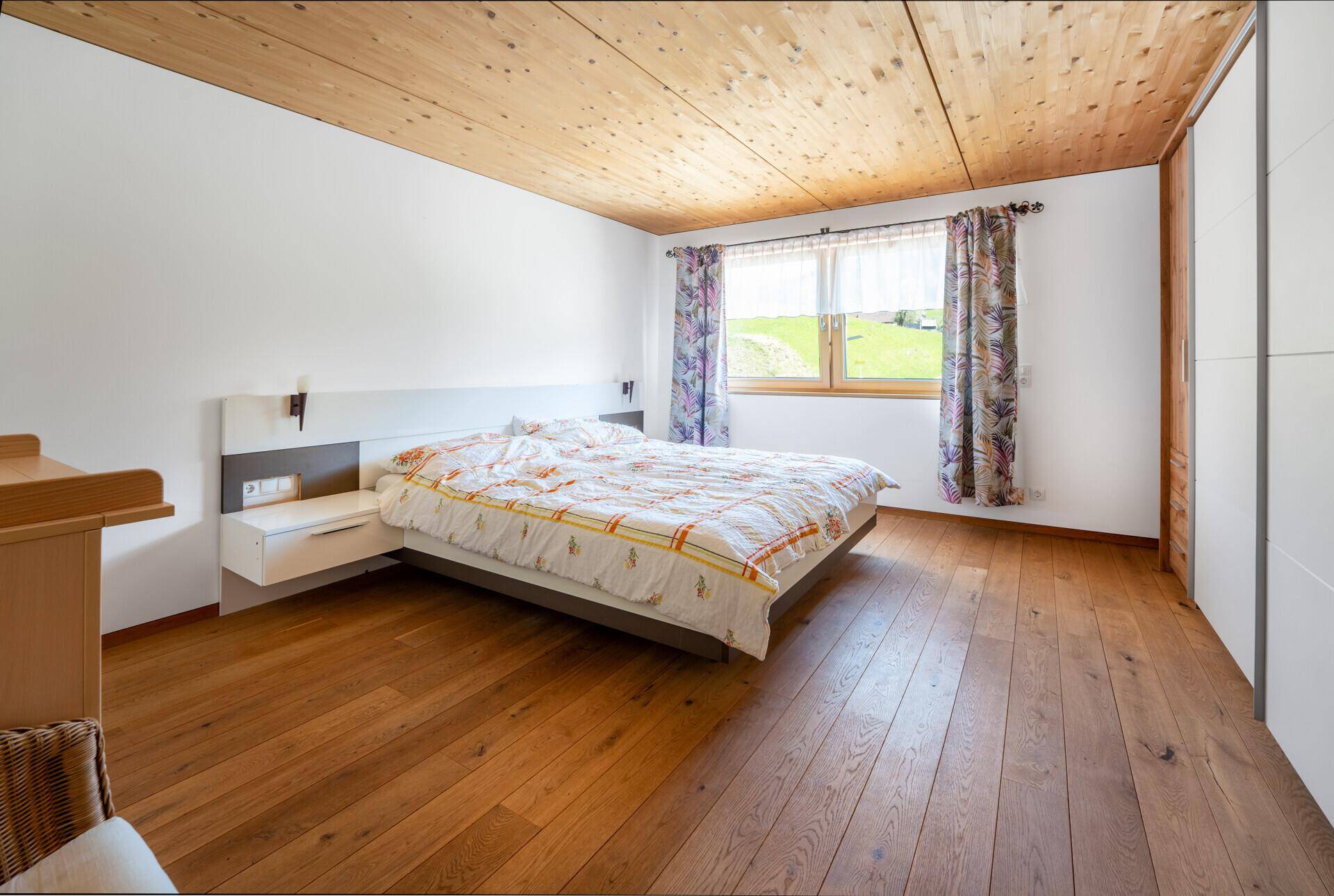 Schlafzimmer mit Doppelbett, Holzdielenboden und Holzschrägdecke, bietet einen Blick ins Grüne.
