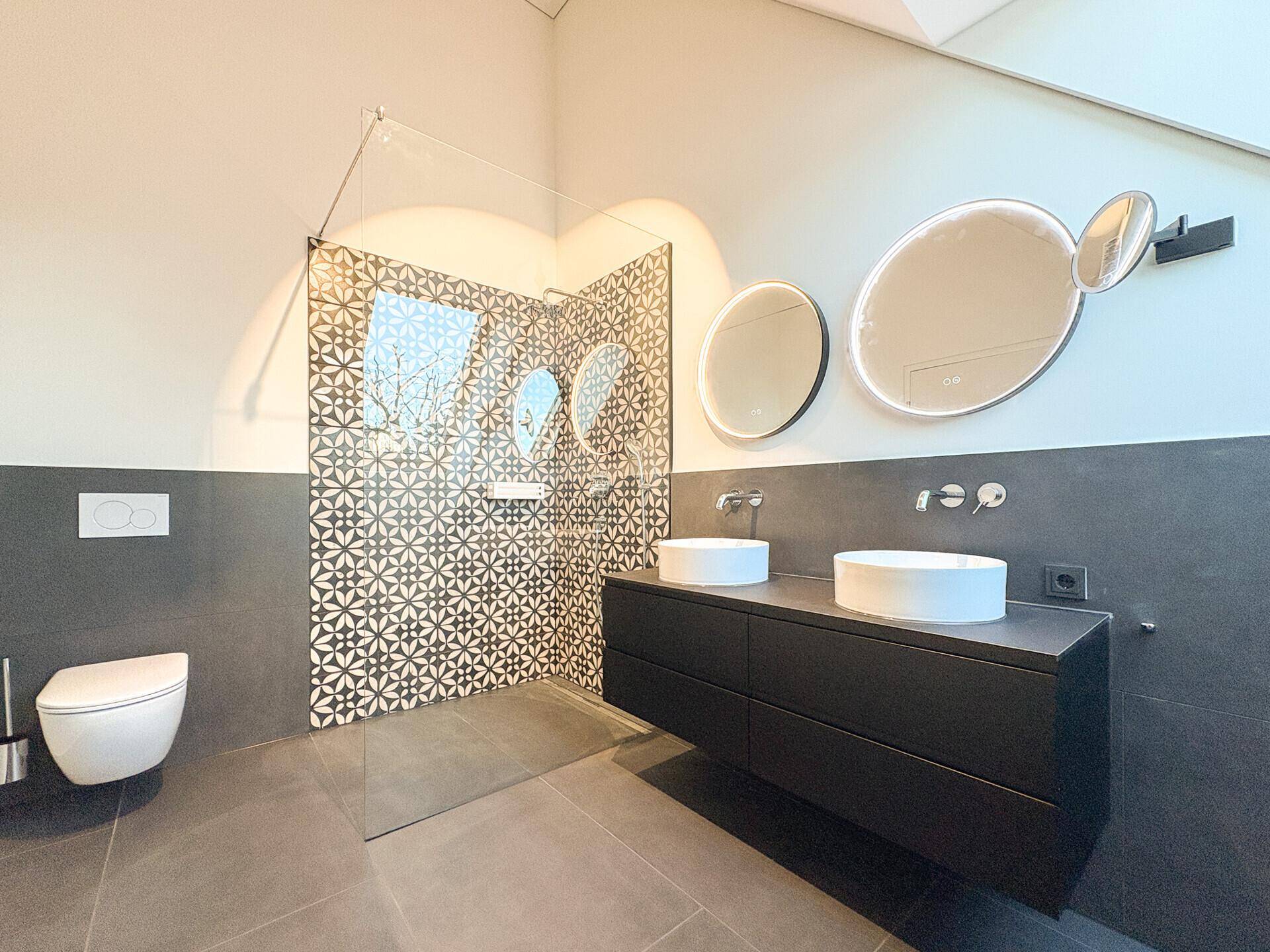Modernes Badezimmer mit begehbarer Dusche, Doppelwaschbecken und stilvollen Fliesen an der Wand.