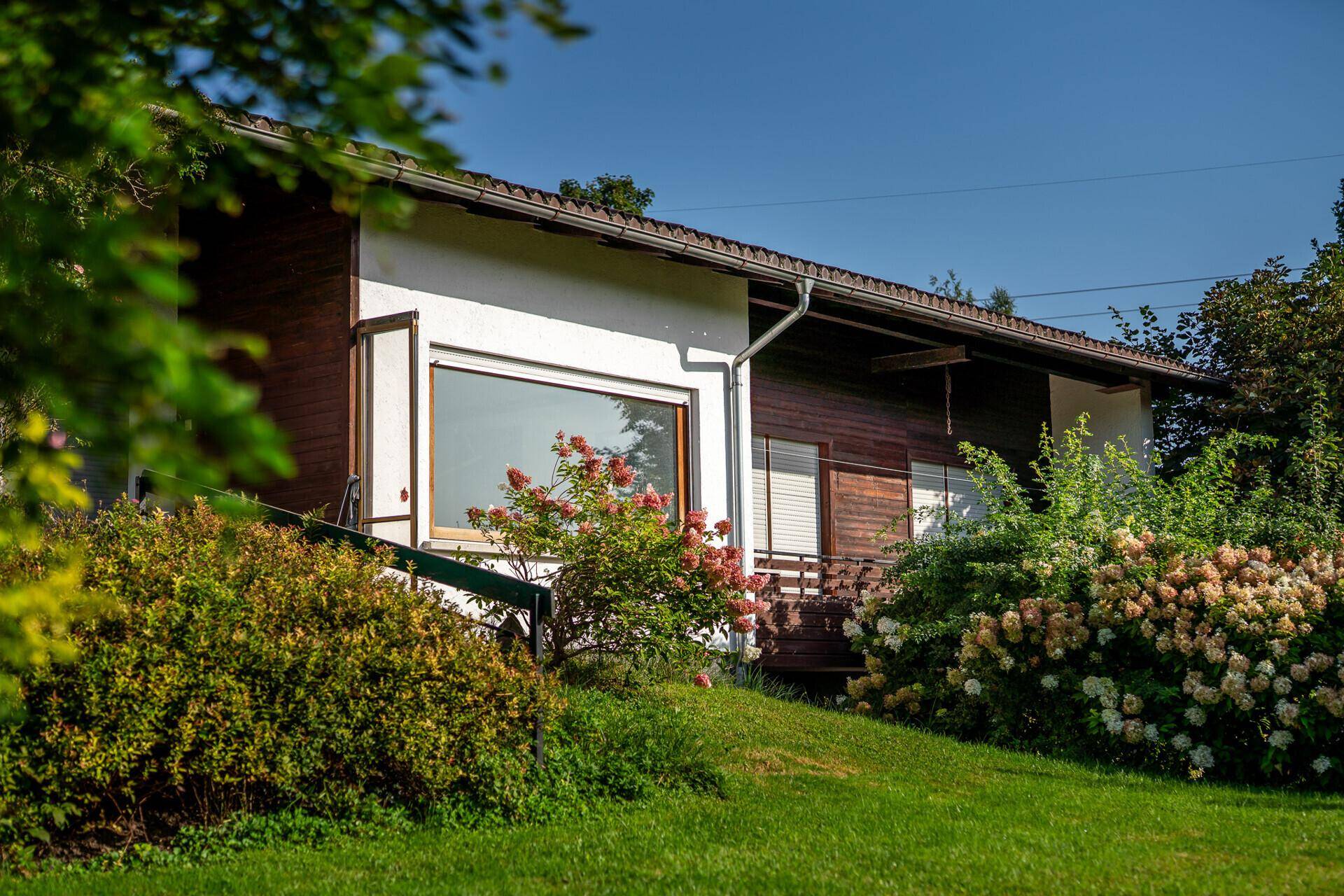 Seitenansicht des Hauses mit großer Fensterfront und gepflegtem Vorgarten.