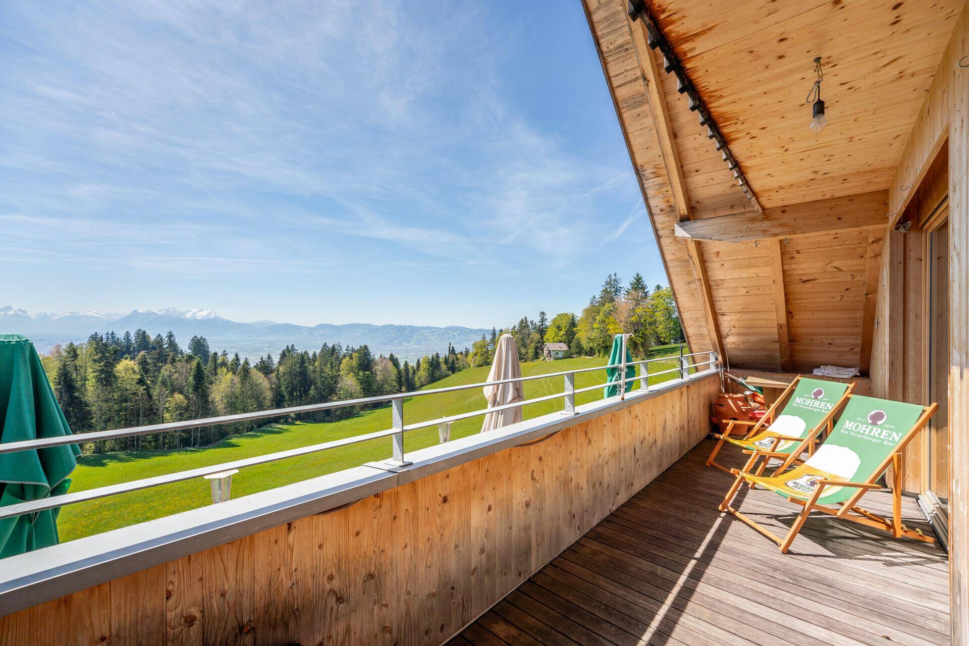 Weiterer Blick auf den Holzbalkon mit mehreren Liegestühlen und der beeindruckenden Berg- und Landschaftsaussicht.