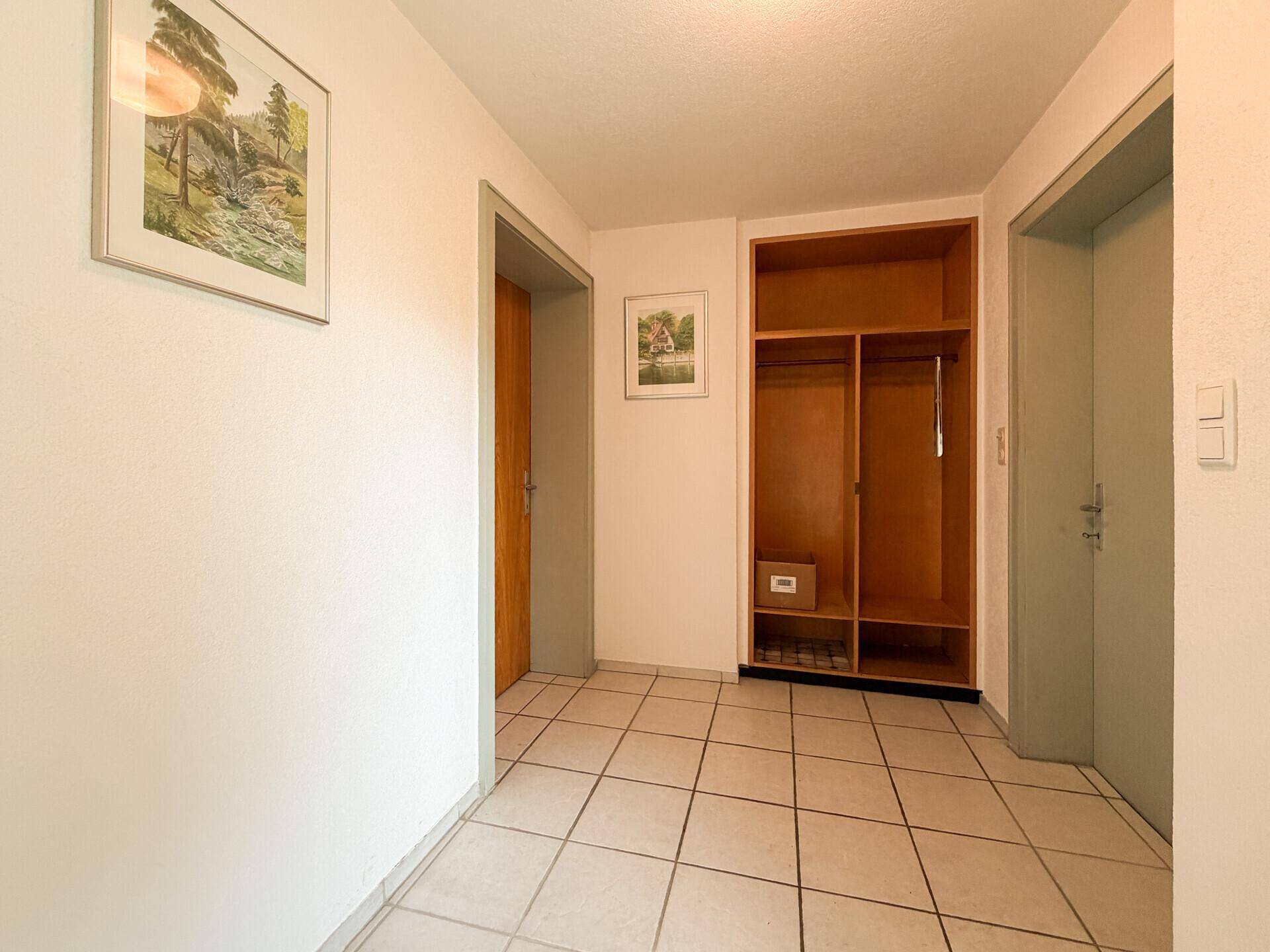 Geräumiger Flur mit Fliesenboden und einem offenen Holzregal für Garderobe.