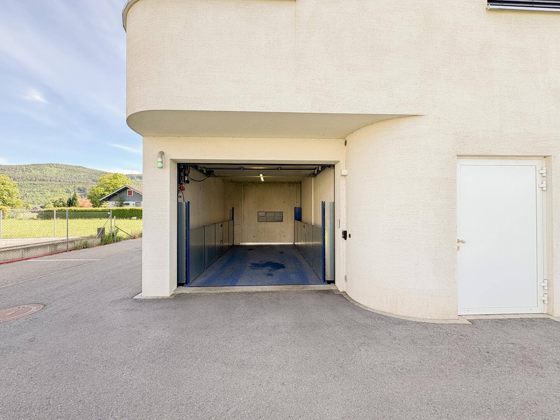 Eingang zur Tiefgarage mit Autolift und moderner Fassade des Gebäudes.
