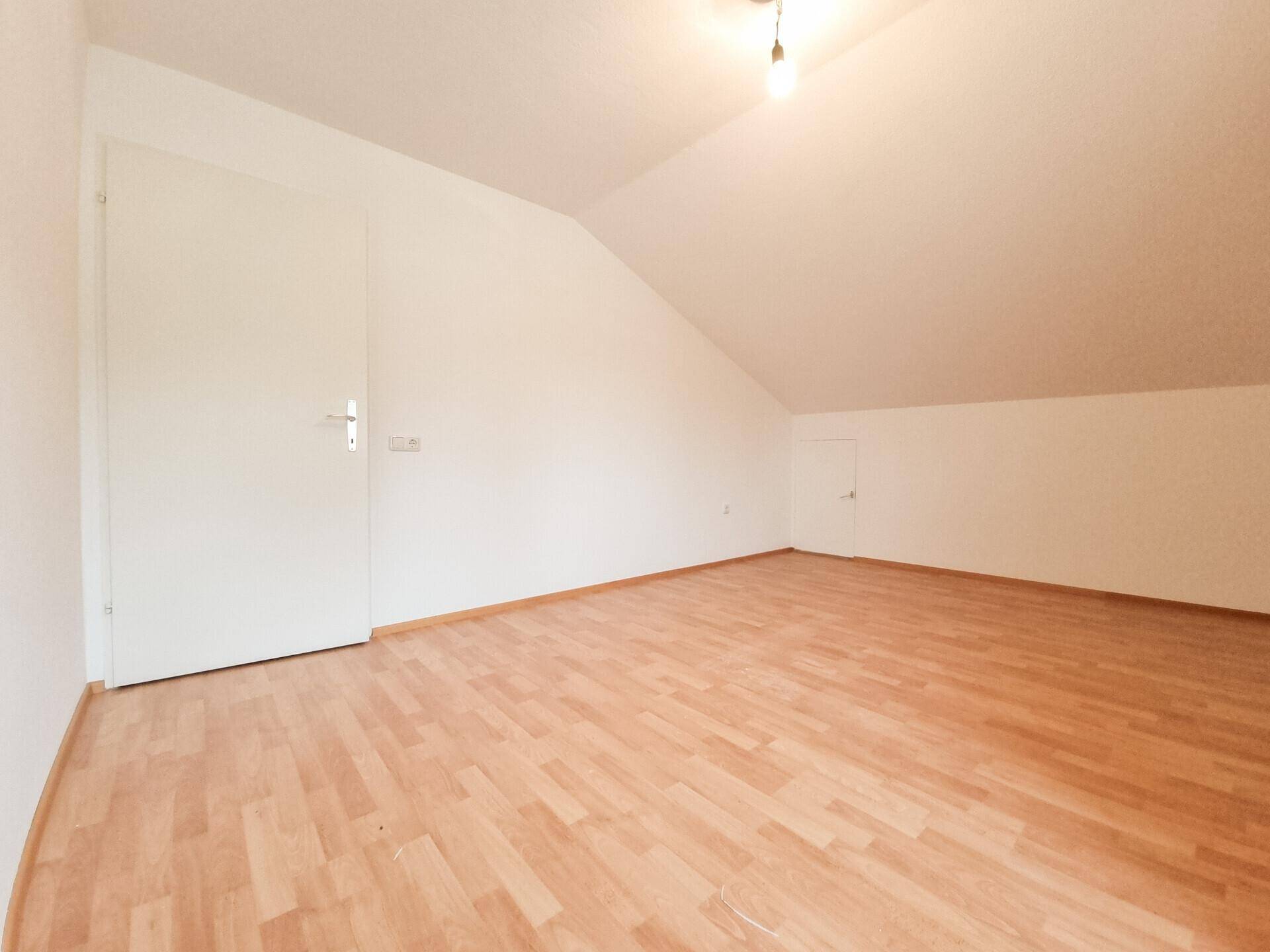 Leerer Raum mit Dachschräge und Laminatboden, bereit für individuelle Gestaltung.