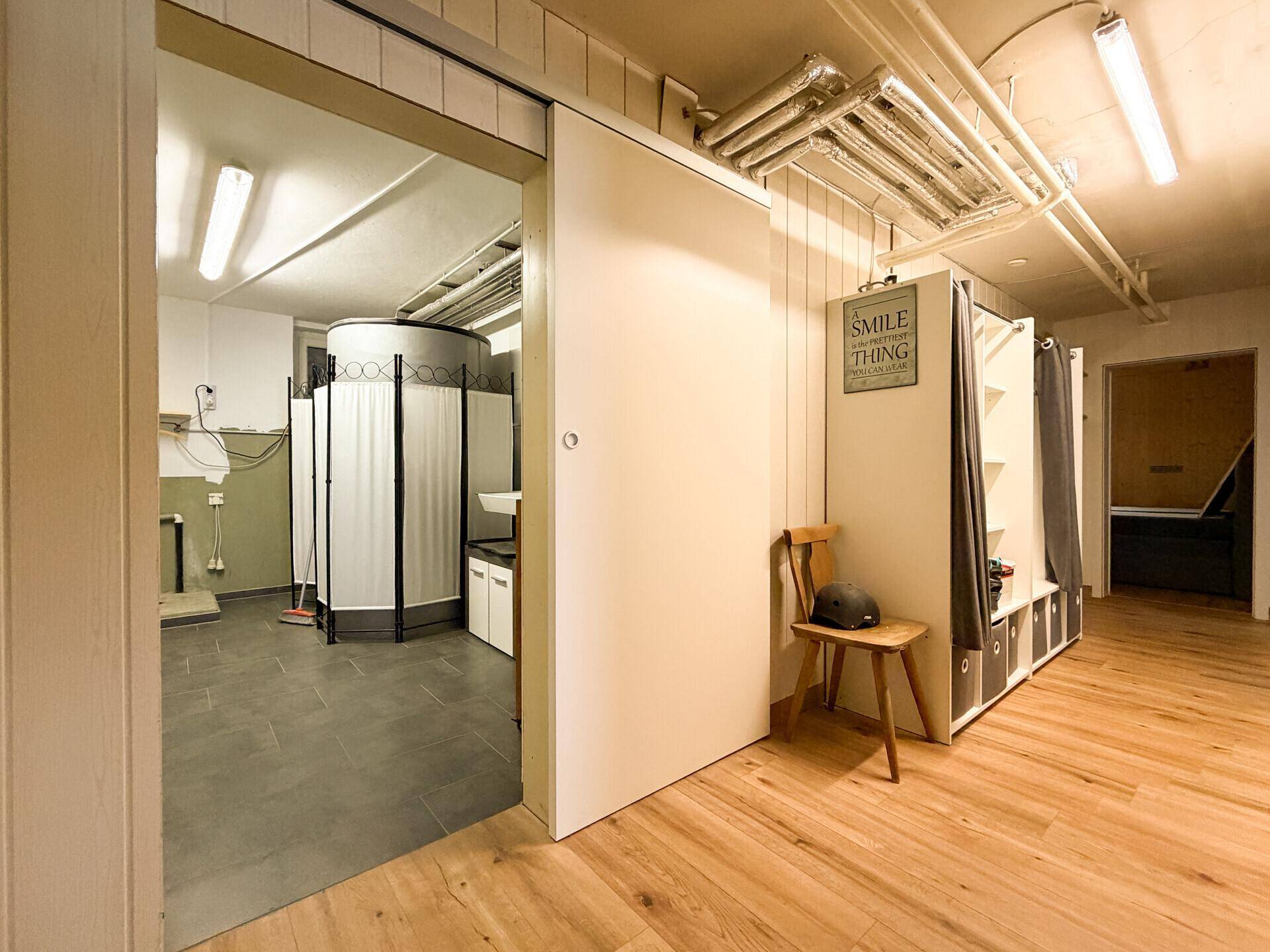Geräumiger Hauswirtschaftsraum mit Holz- und Fliesenboden, Waschbecken und offenliegenden Rohren an der Decke.