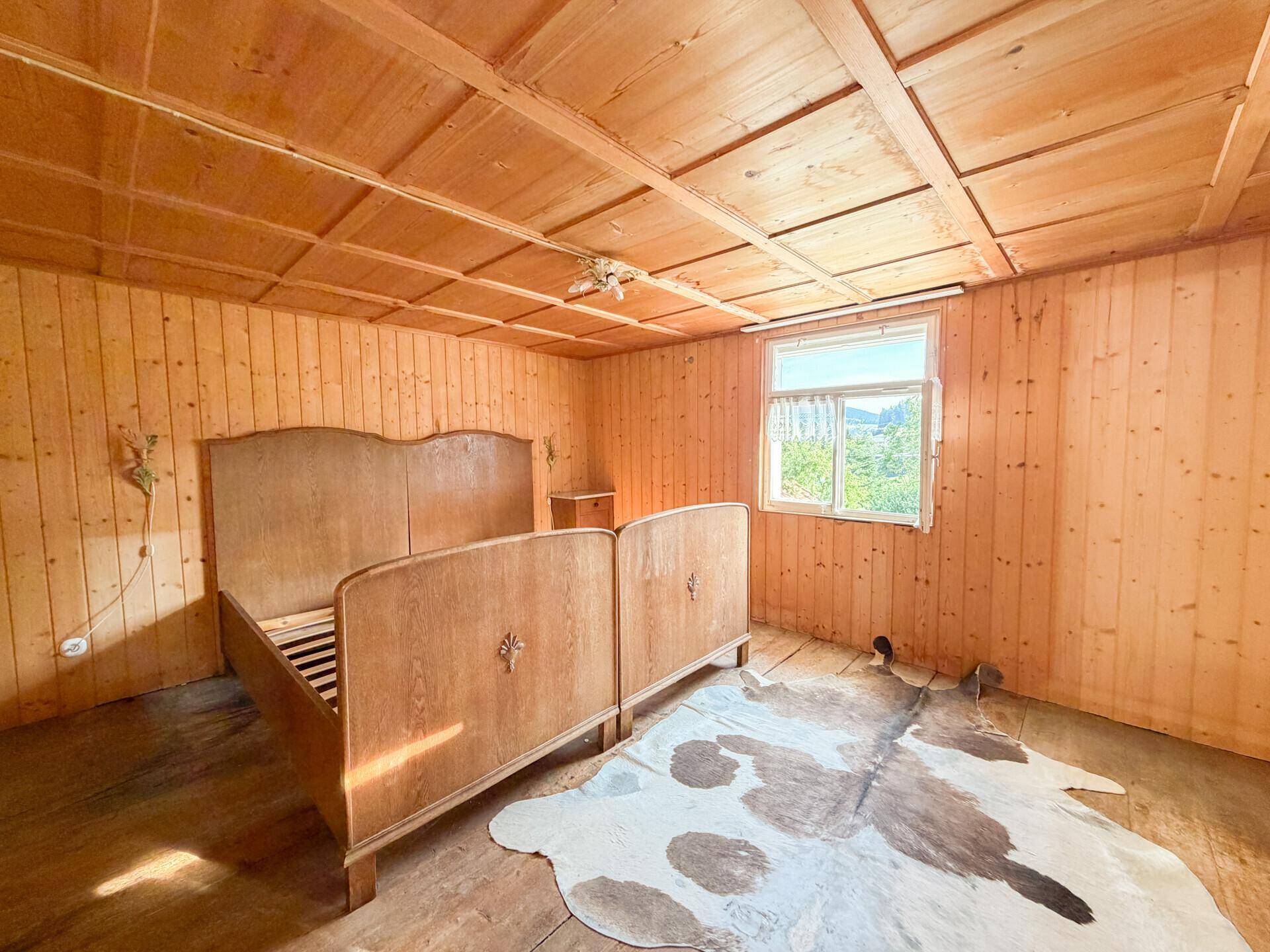 Schlafzimmer im Landhausstil mit Holzbett, Holztäfelung und einem Kuhfellteppich auf dem Boden.