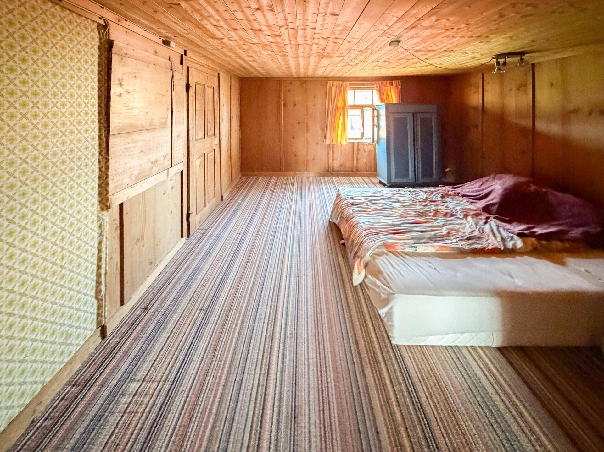 Schlafzimmer mit Holztäfelung, gestreiftem Teppich und einem Fenster, das Tageslicht hereinlässt.