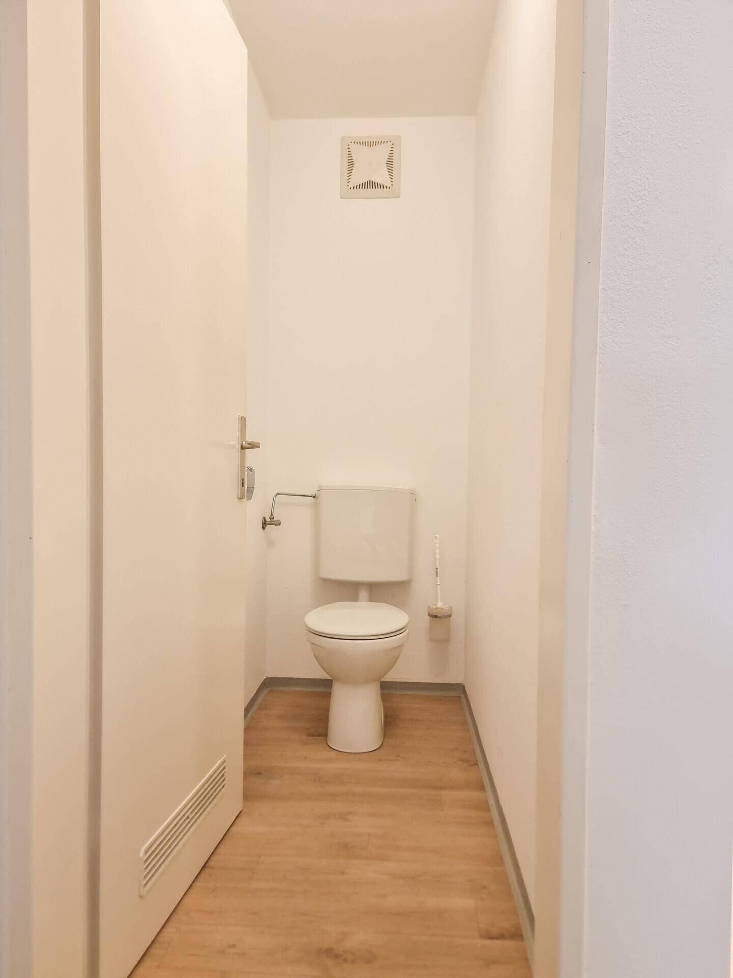 Separate Gästetoilette mit WC und Lüftungsgitter, ausgestattet mit Laminatboden.