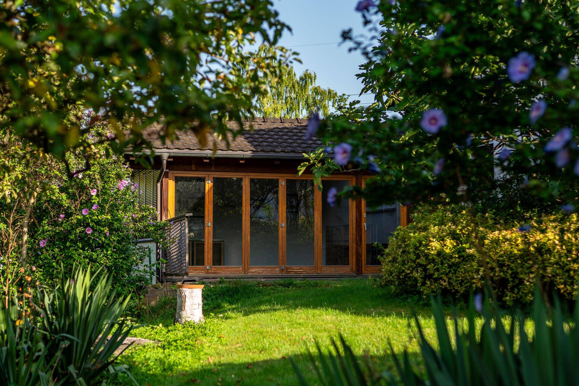 Außenansicht des Wintergartens, umgeben von üppiger Gartenbepflanzung.
