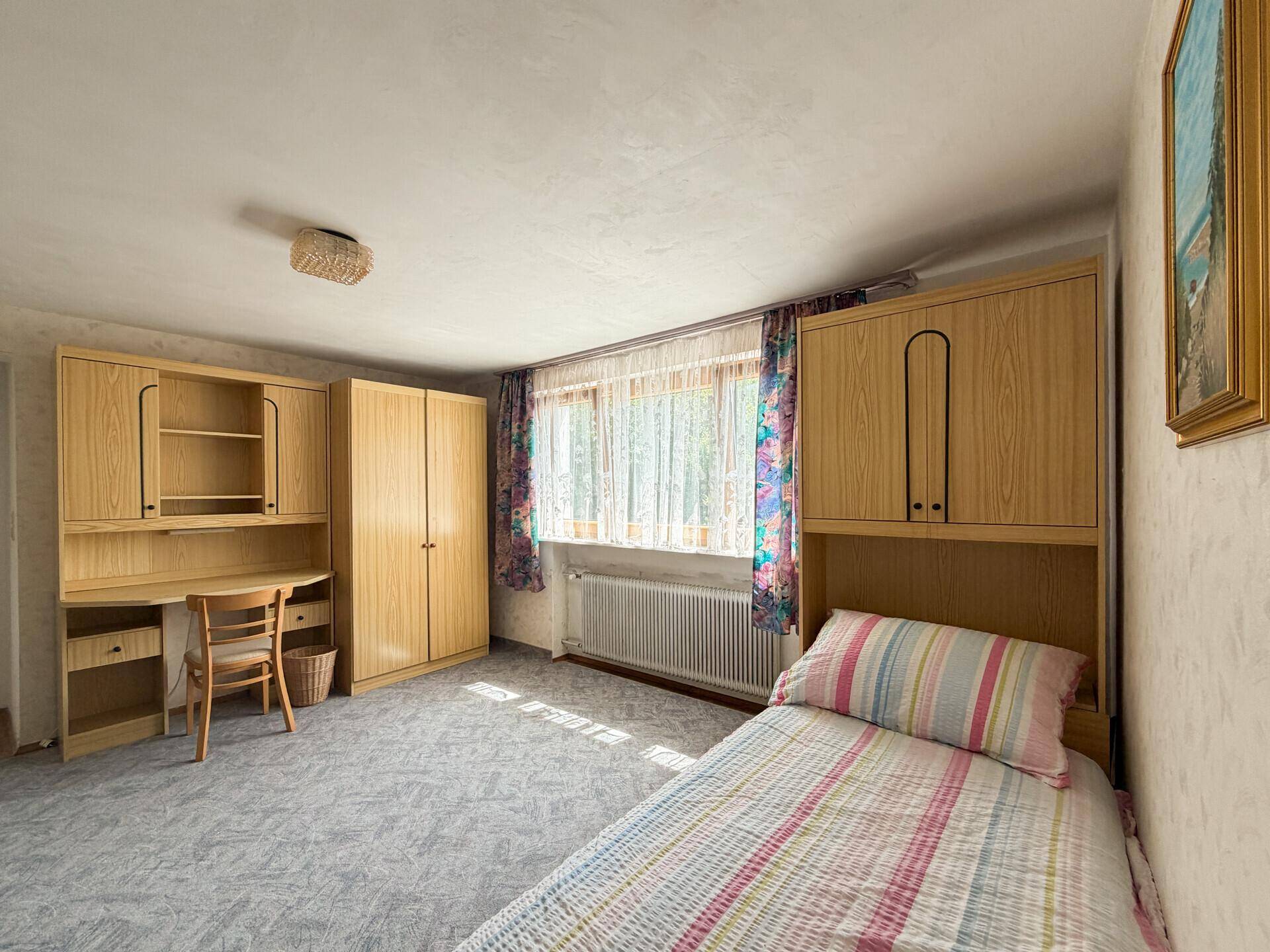 Kinderzimmer mit Teppichboden, Holzmöbeln und einem Einzelbett, hell und funktional eingerichtet.