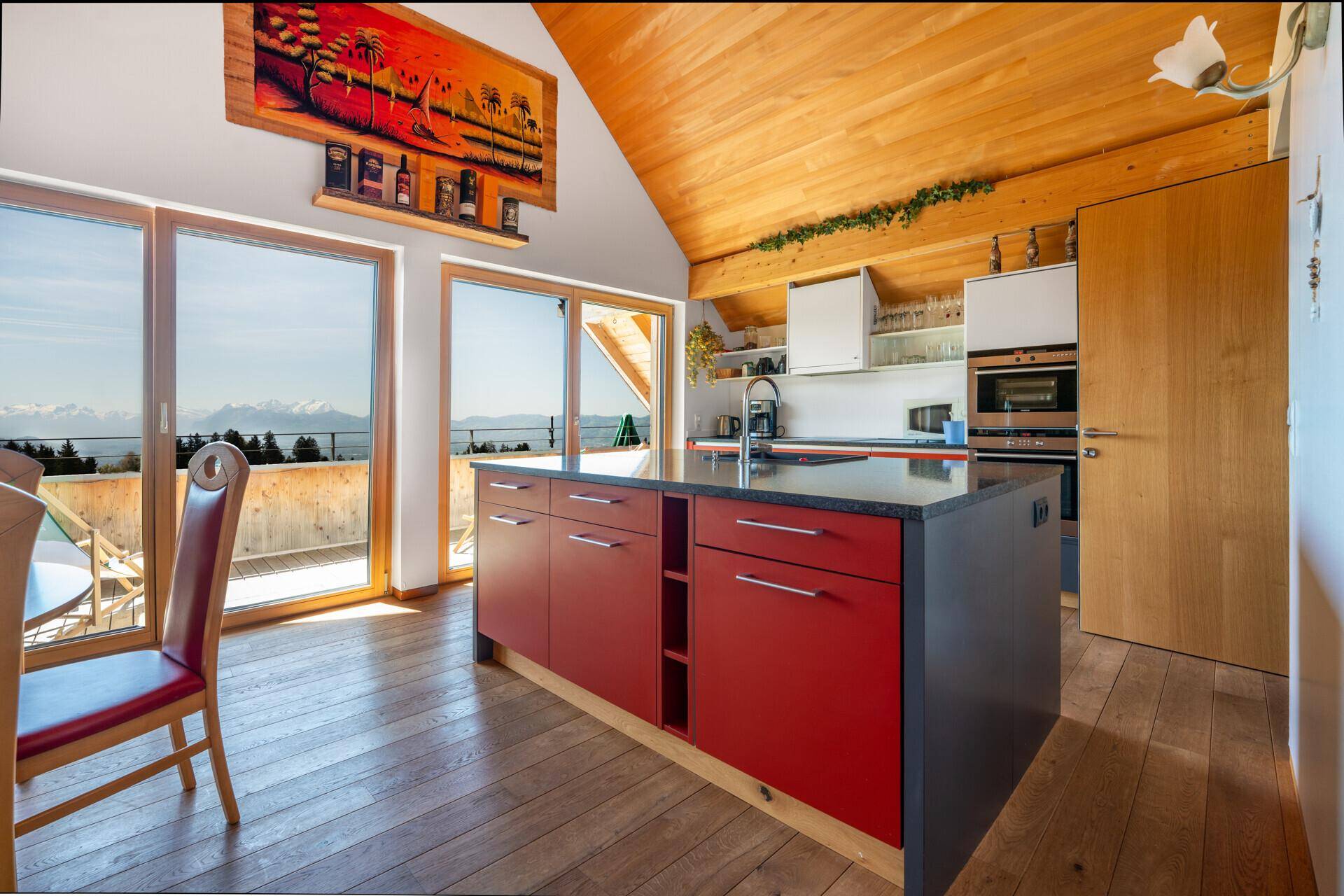 Moderne Küche mit roter Kücheninsel, Einbaugeräten und Holzdachschräge, bietet Bergblick.