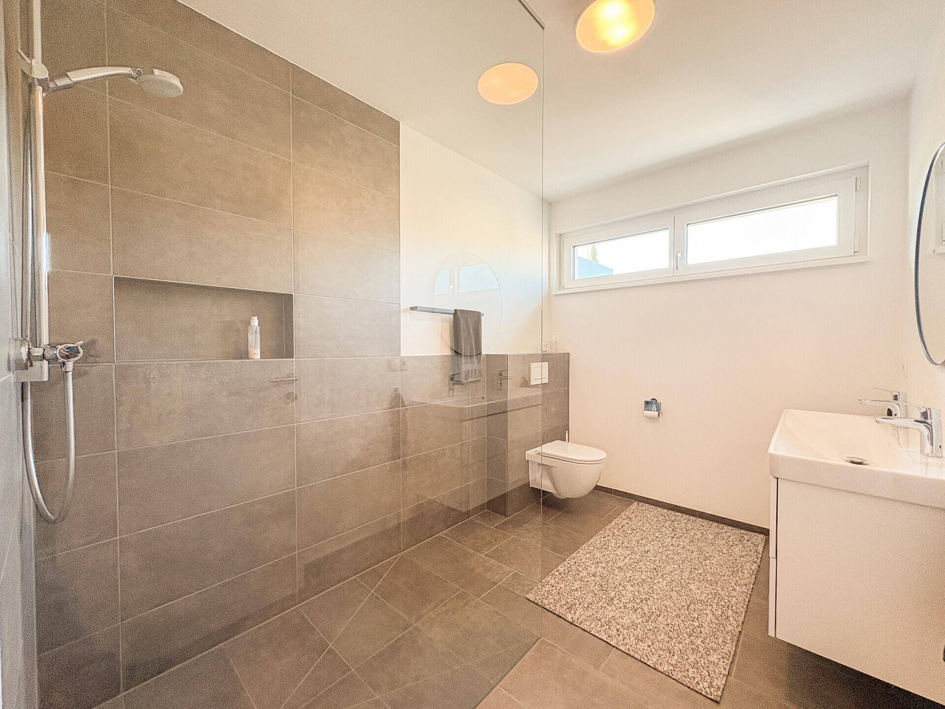 Modernes Badezimmer mit ebenerdiger Dusche, Wand-WC und großem Fenster.