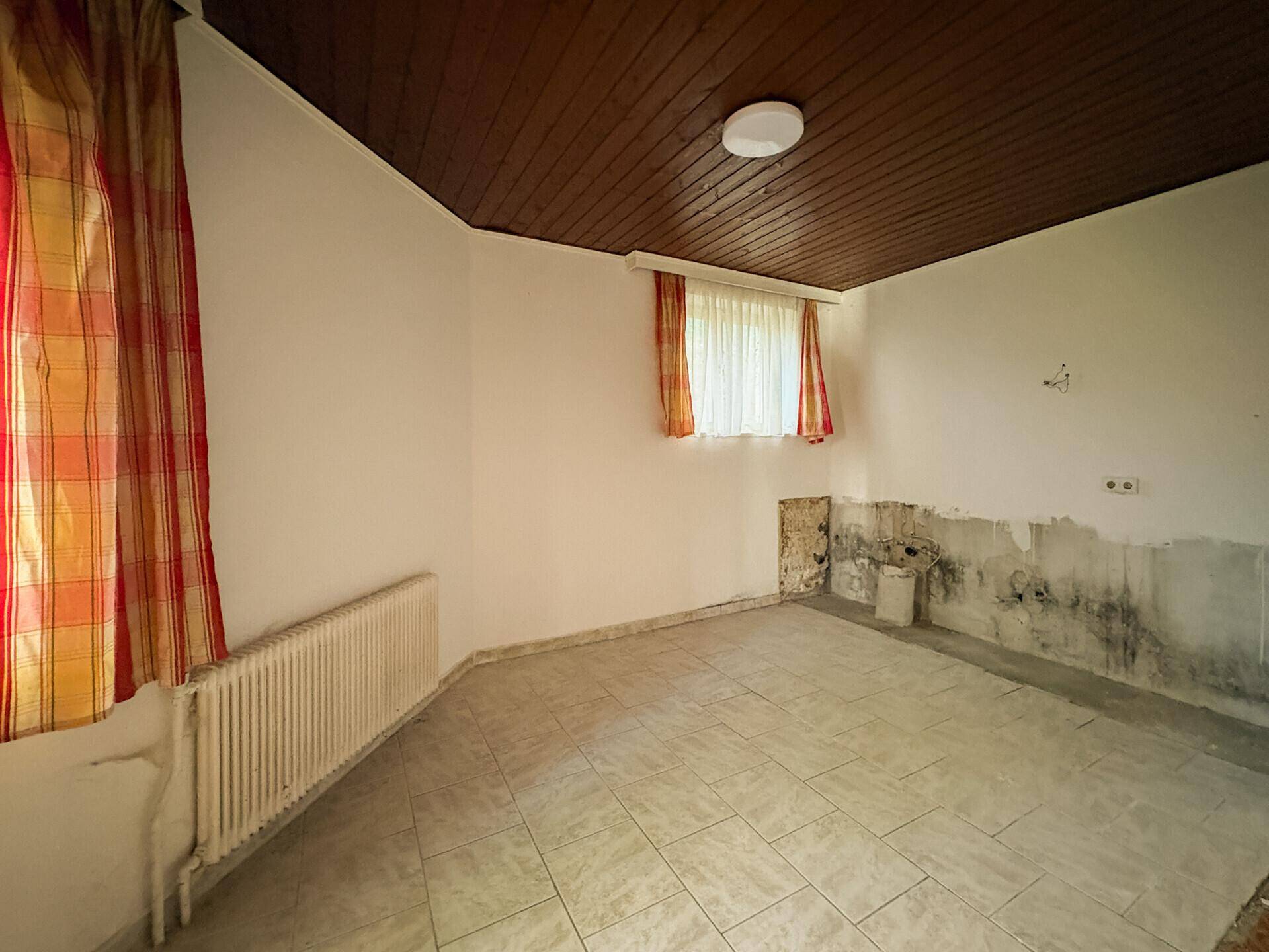 Raum mit Fliesenboden und sichtbaren Feuchtigkeitsschäden an den Wänden, renovierungsbedürftig.