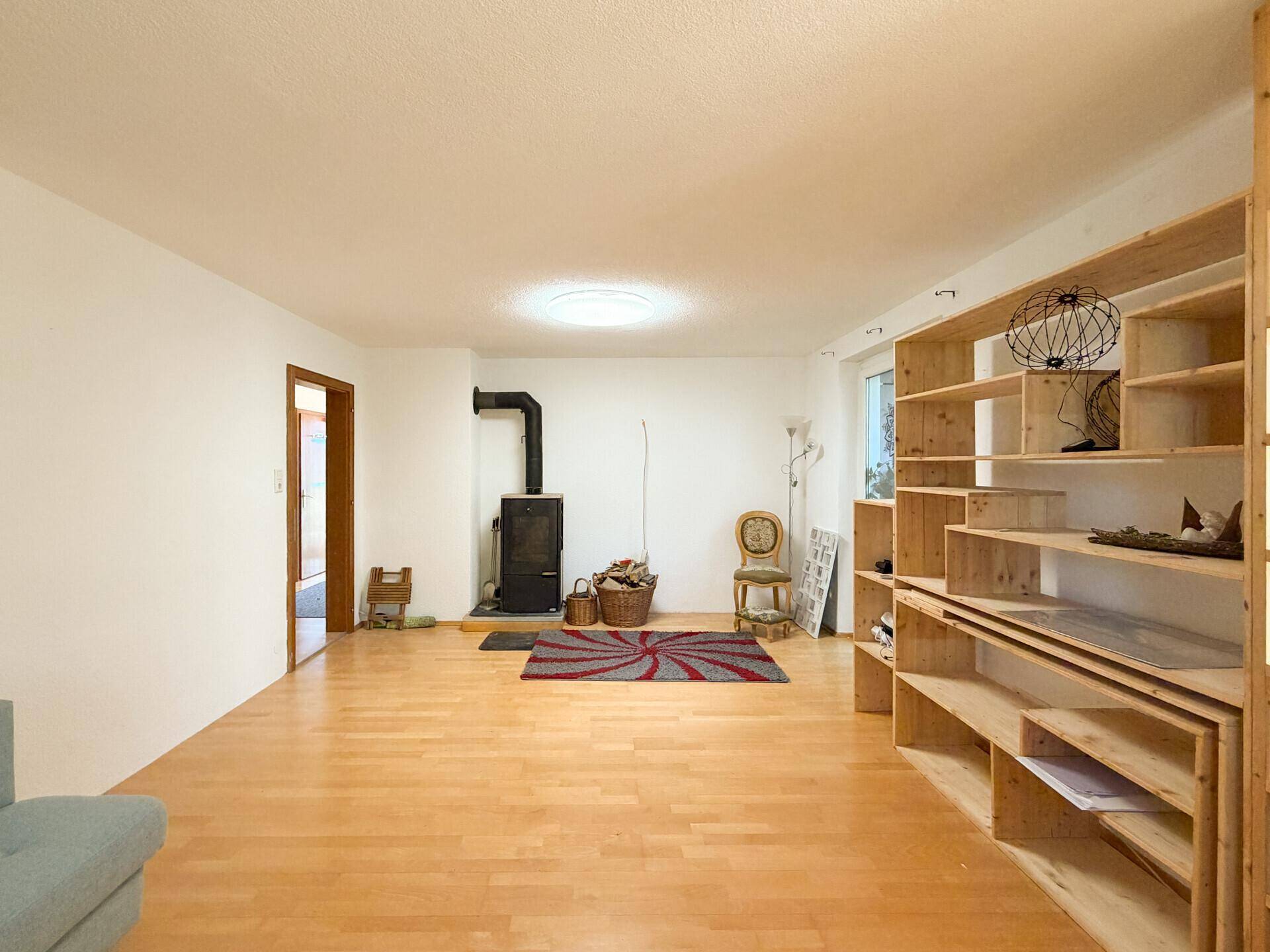 Gemütliches Wohnzimmer mit Holzparkett, einem Kaminofen und integrierten Holzregalen, ideal für entspannte Abende.