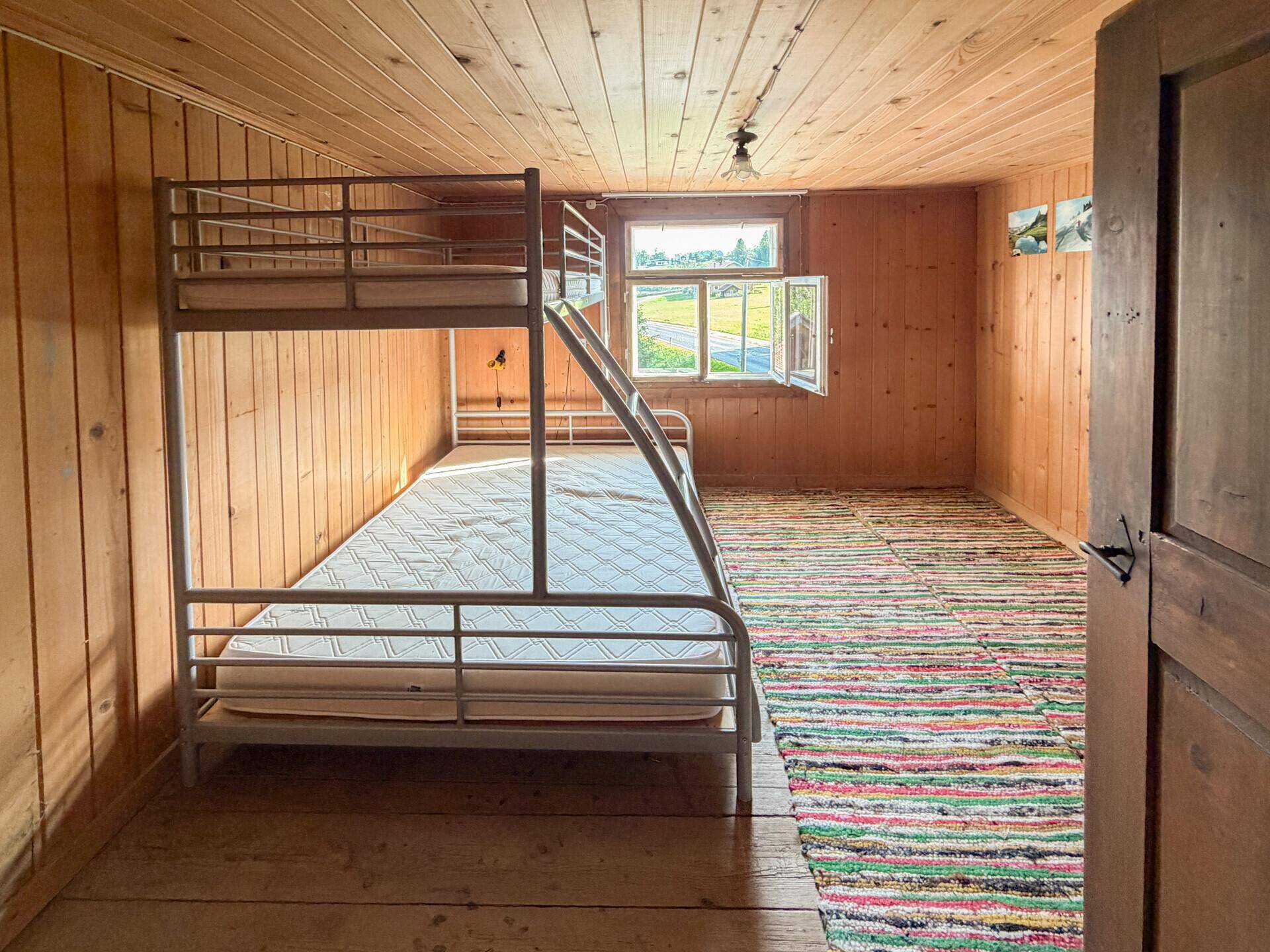 Kinderzimmer mit Etagenbett, Holzwänden und einem bunten Teppich auf dem Holzboden.