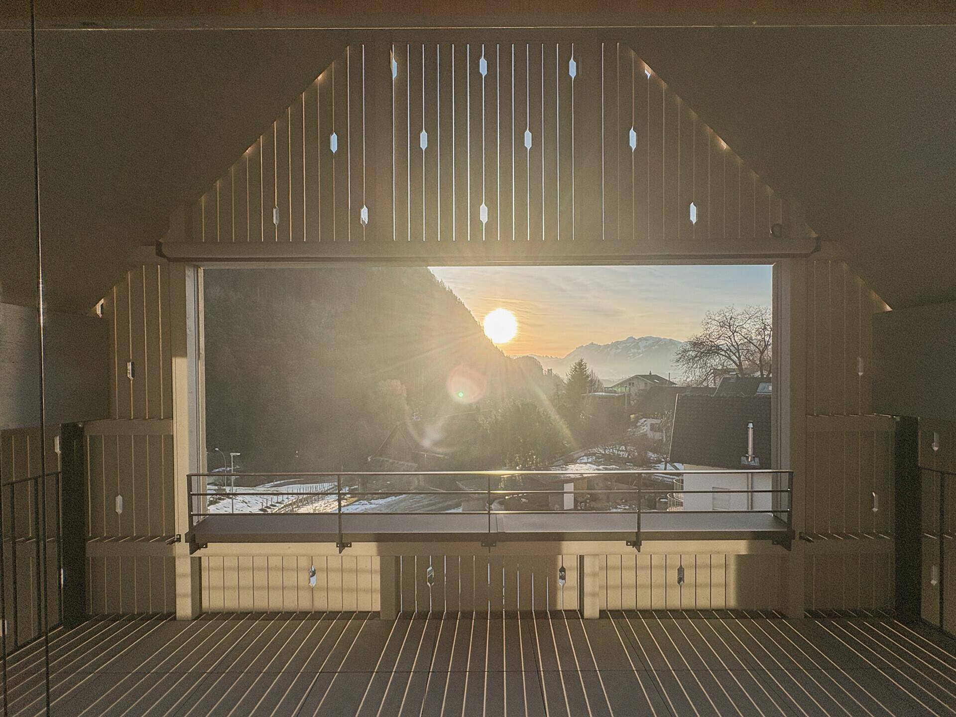 Heller Raum mit großer Fensterfront und beeindruckendem Blick auf die Berglandschaft bei Sonnenuntergang.
