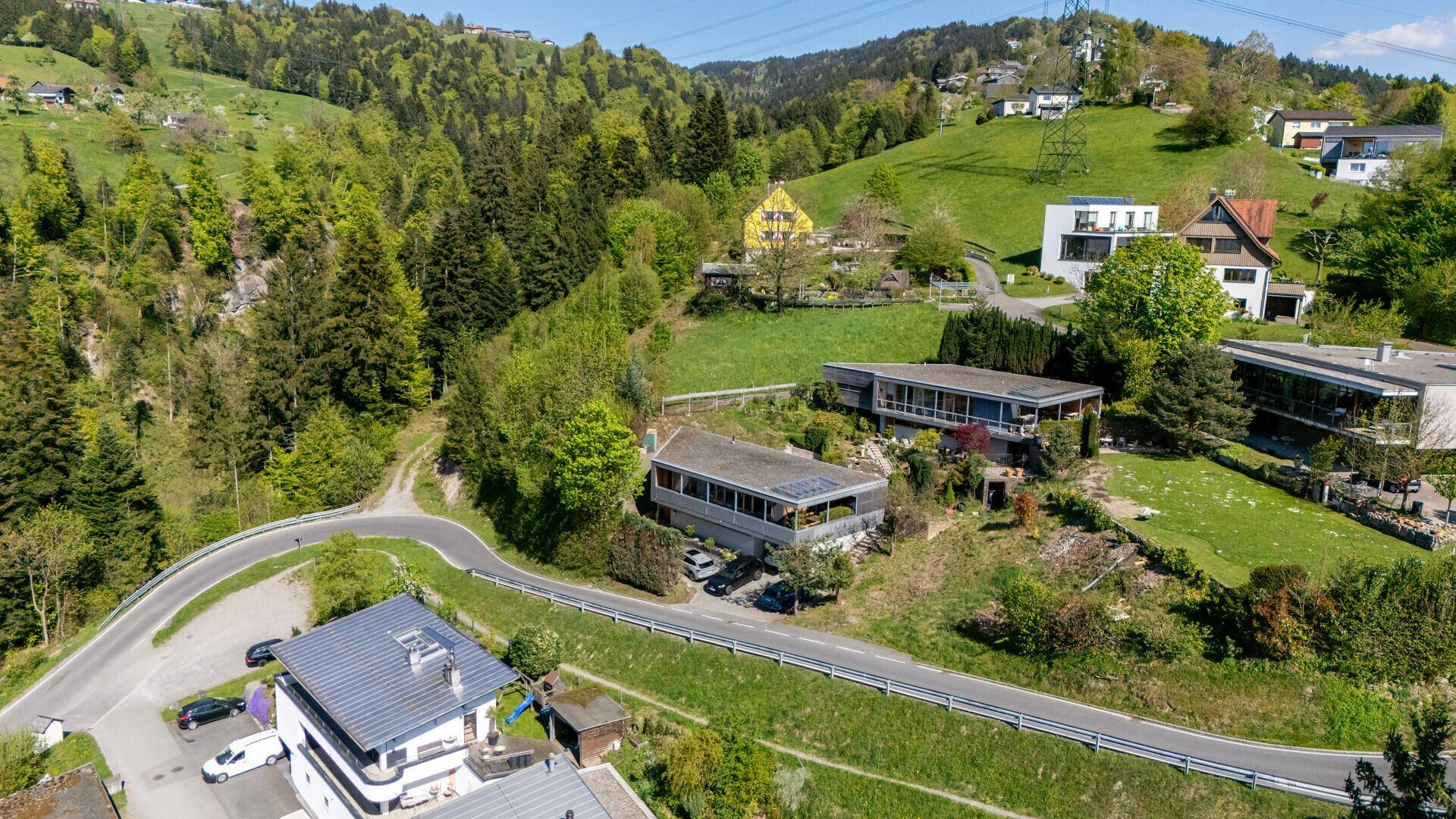 Luftaufnahme einer Wohnsiedlung am Hang mit viel Grün und einer kurvenreichen Straße.