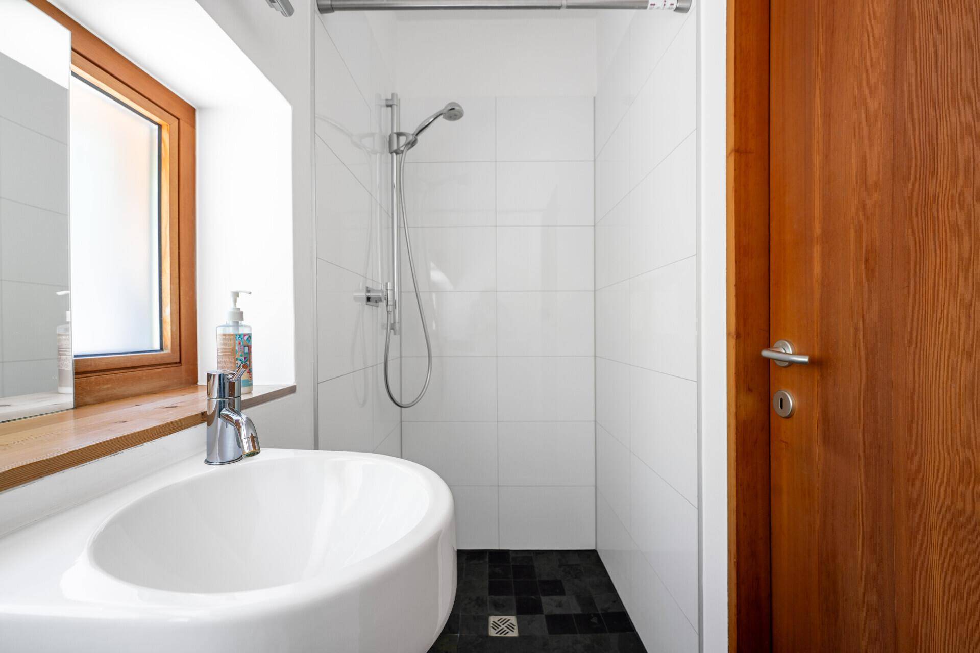 Modernes Duschbad mit Waschbecken, Duschbereich und Fenster.