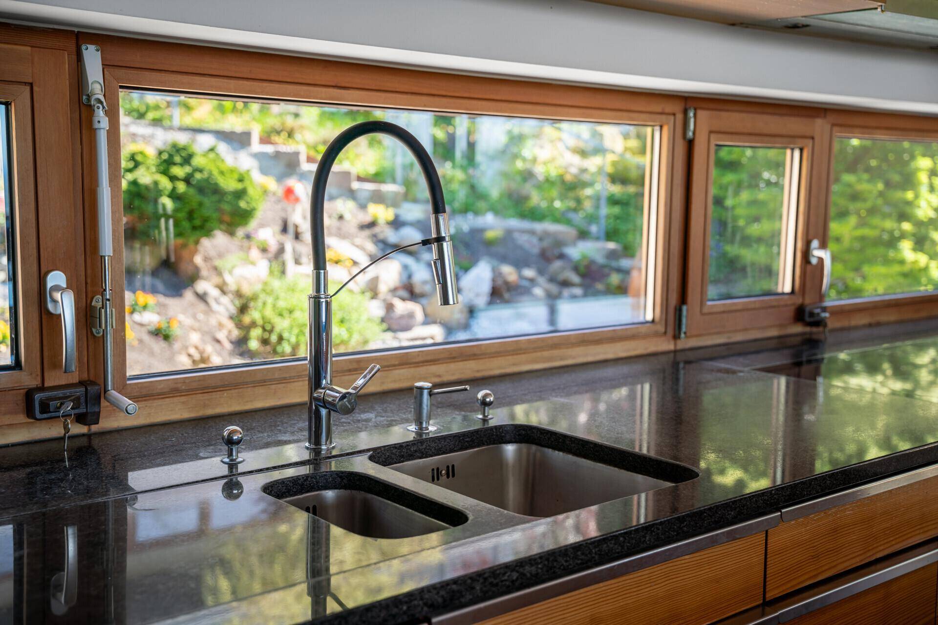 Detailansicht der modernen Küchenspüle mit flexiblem Wasserhahn und Gartenblick.