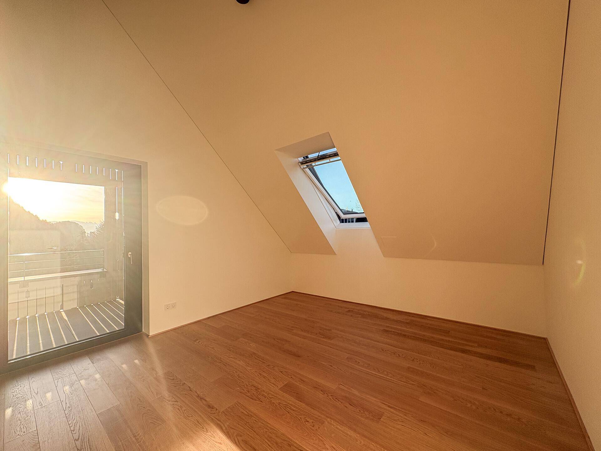 Helles Dachzimmer mit Holzboden, Dachfenster und französischem Balkon für viel Tageslicht.