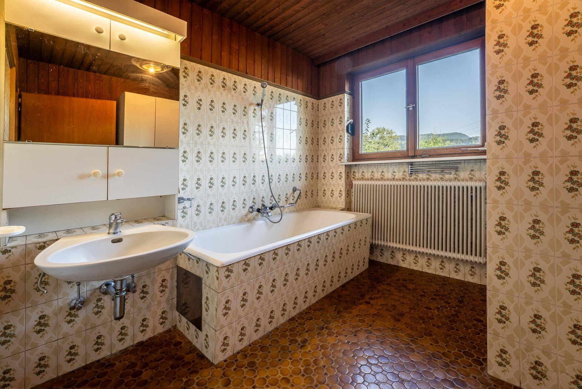 Badezimmer im 80er-Jahre-Stil mit gemusterten Fliesen, Badewanne und Fenster.
