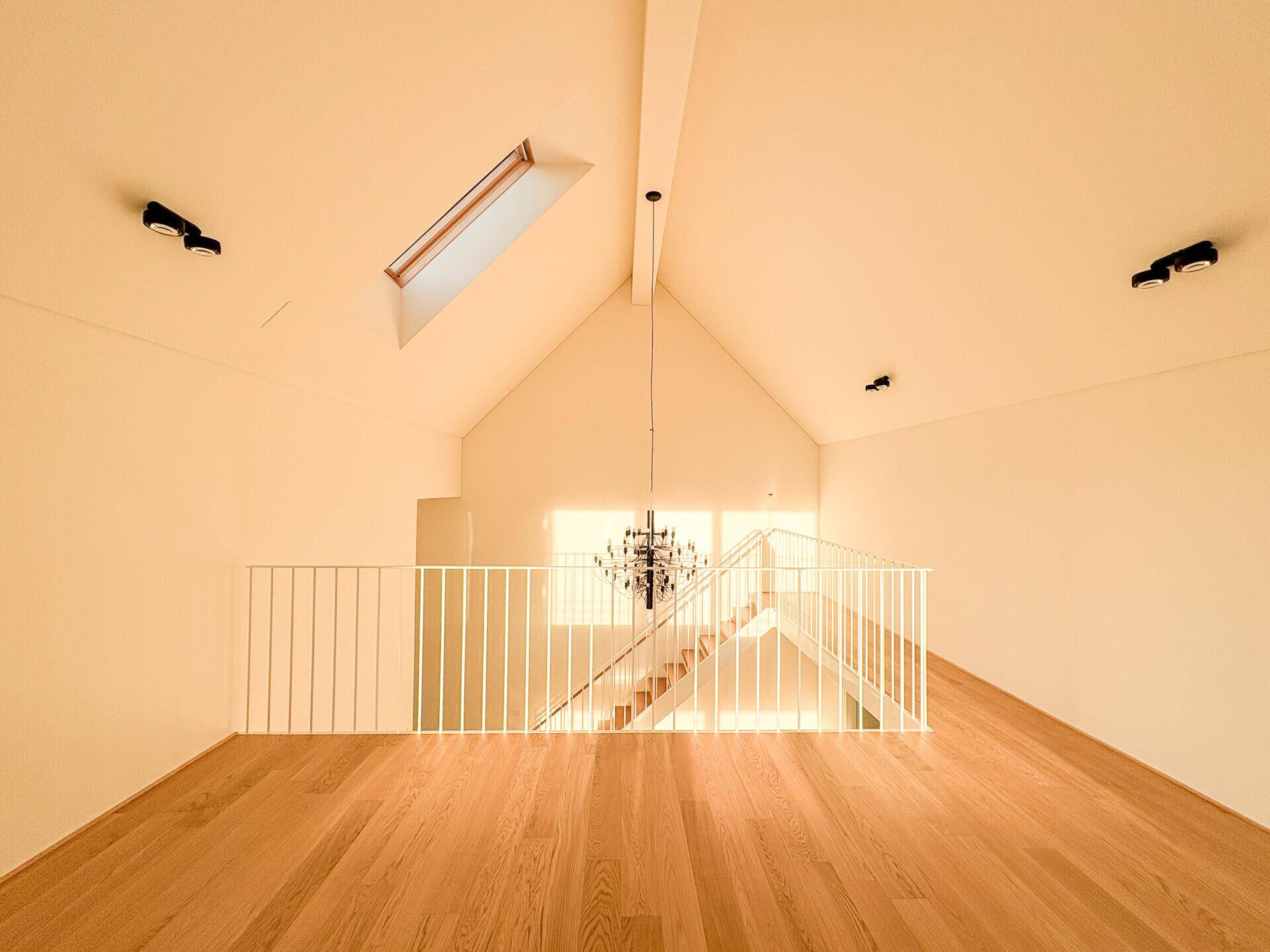 Heller Galeriebereich im Dachgeschoss mit Holzboden, Dachschräge und einem Dachfenster.
