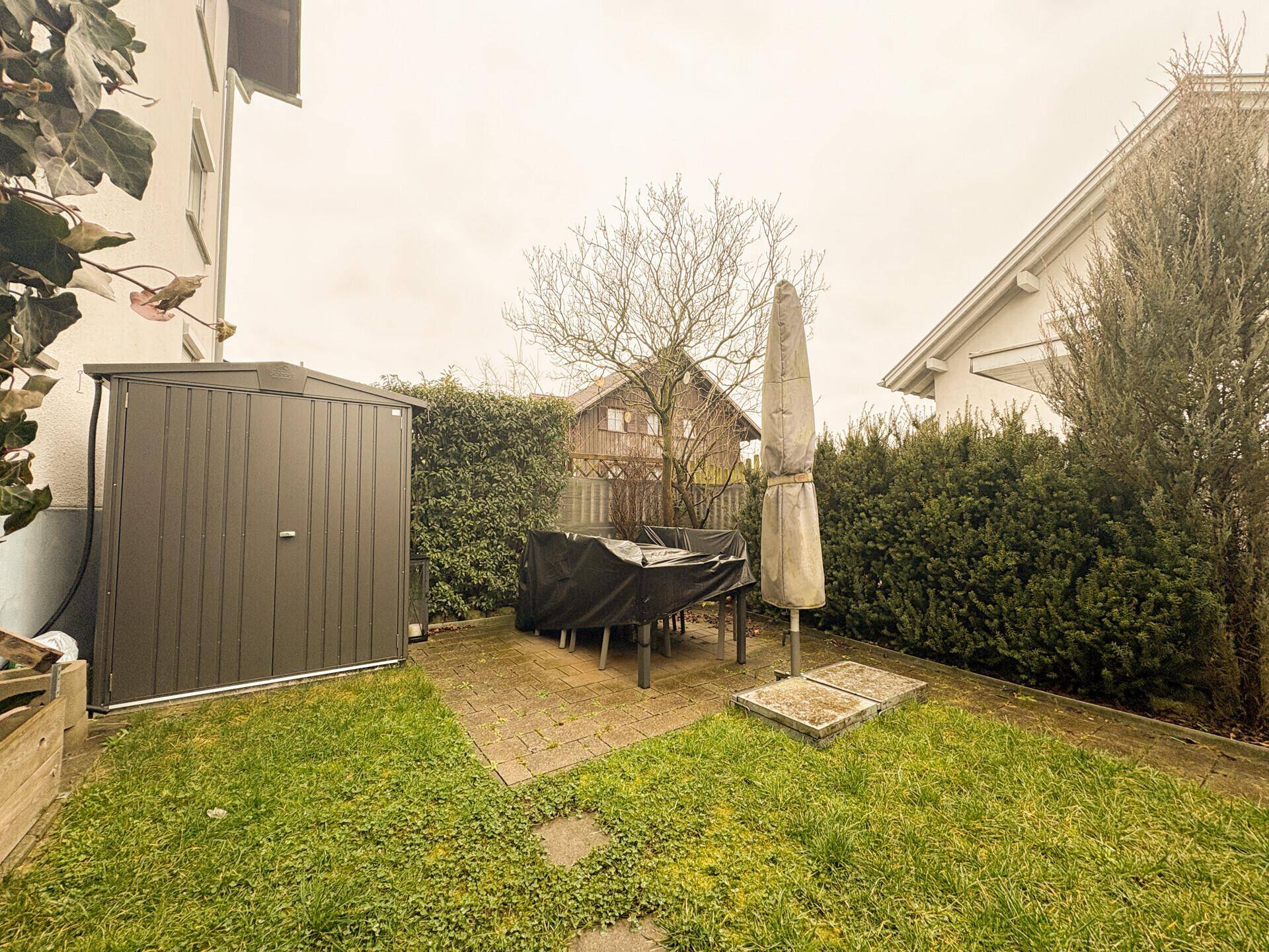 Kleiner Gartenbereich mit Rasenfläche, Sitzgelegenheit und Gartenhaus.