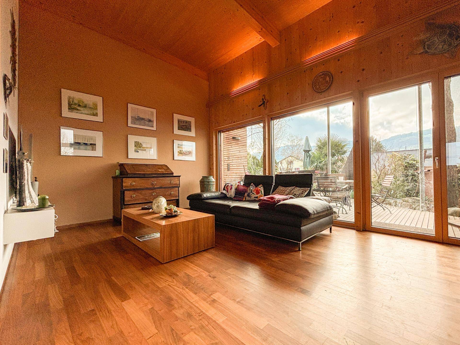 Helles Wohnzimmer mit bequemer Couch, Holzboden und weitem Blick in die Landschaft.