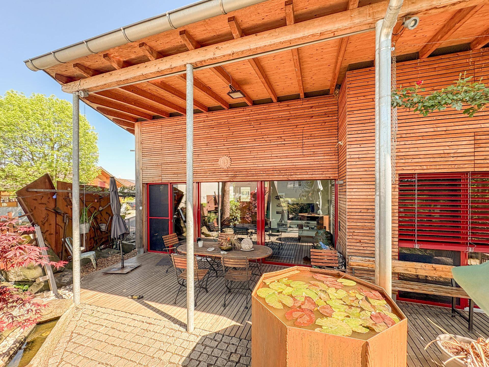 Überdachte Holzterrasse mit Sitzgelegenheiten und einem dekorativen Wasserbecken.