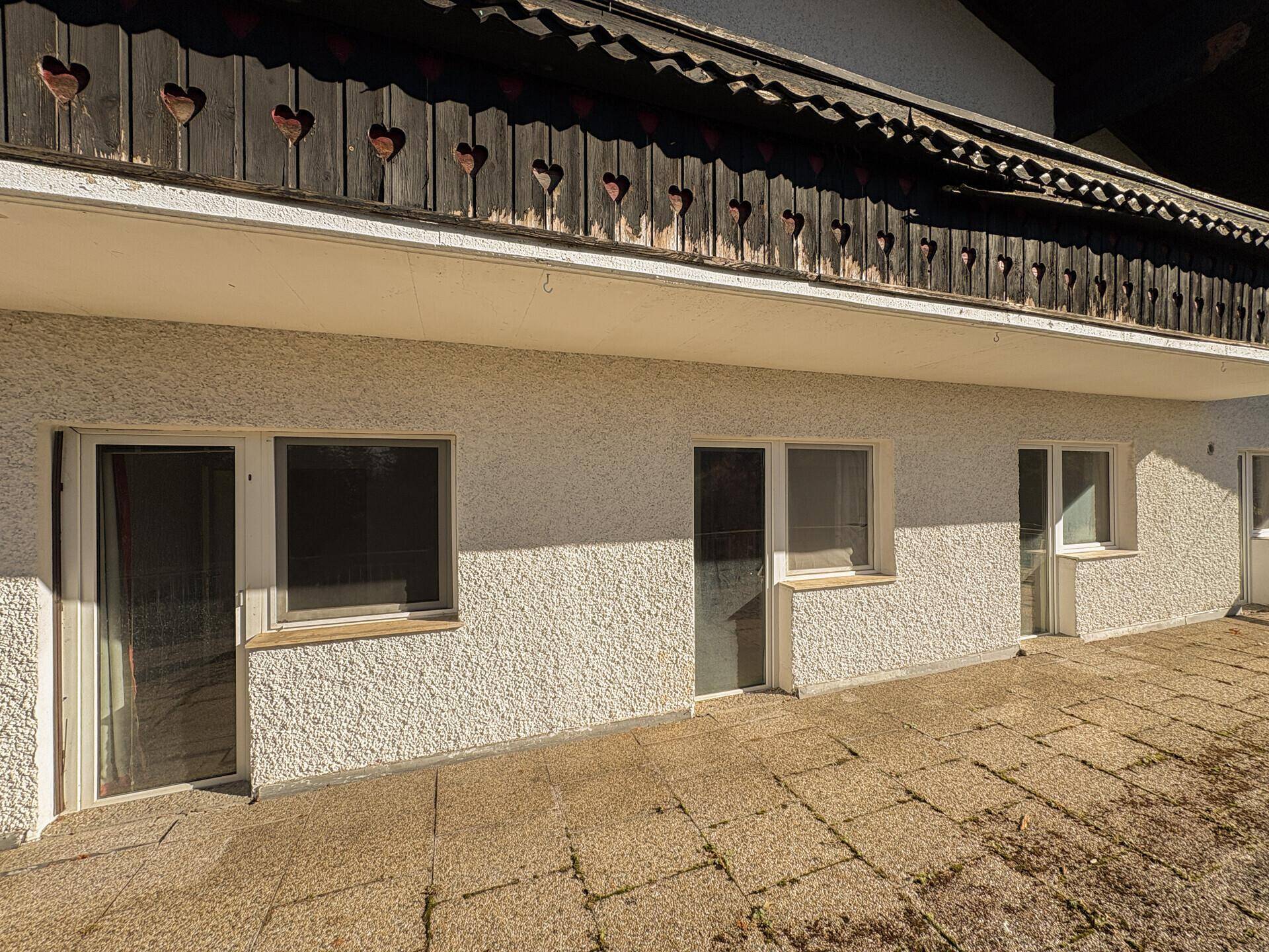 Fassade des Hauses mit mehreren Fenstern und Türen, die zu einer gepflasterten Terrasse führen.